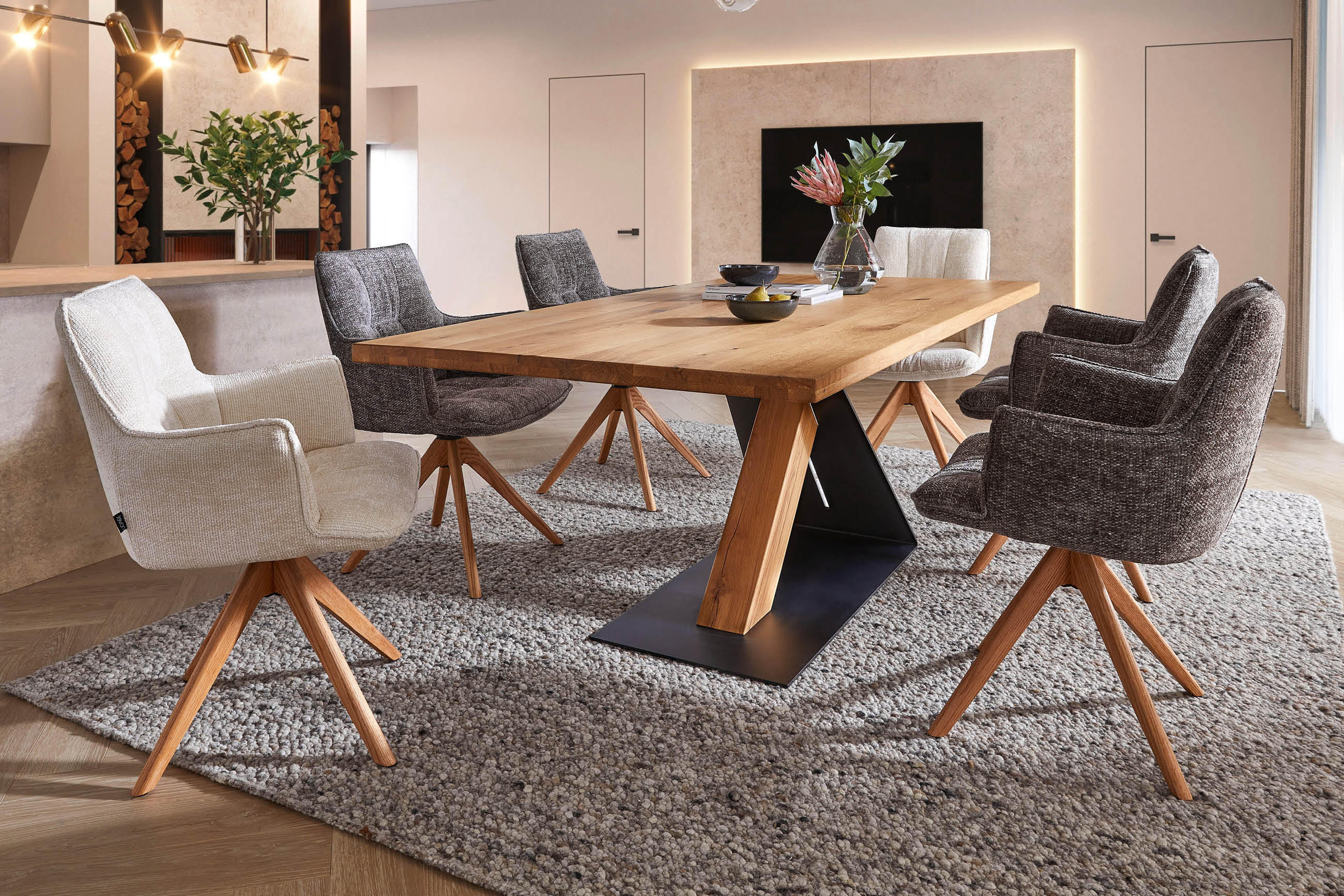 Esszimmertisch aus Holz mit schwarzer Metallbasis umgeben von sechs gepolsterten Stühlen auf grauem Teppich in modernem Raum mit indirekter Wandbeleuchtung