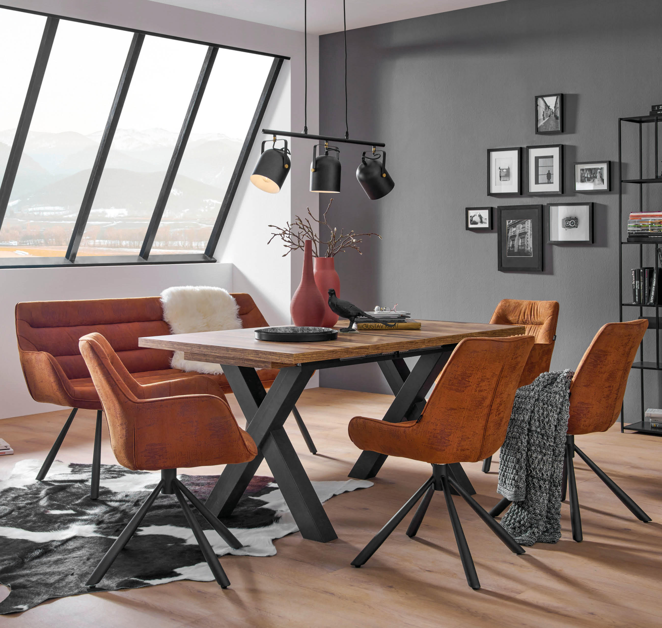 Esszimmer mit braunen Ledersesseln um einen Holztisch auf hellem Holzboden mit Kuhfellteppich und großen Fenstern im Hintergrund