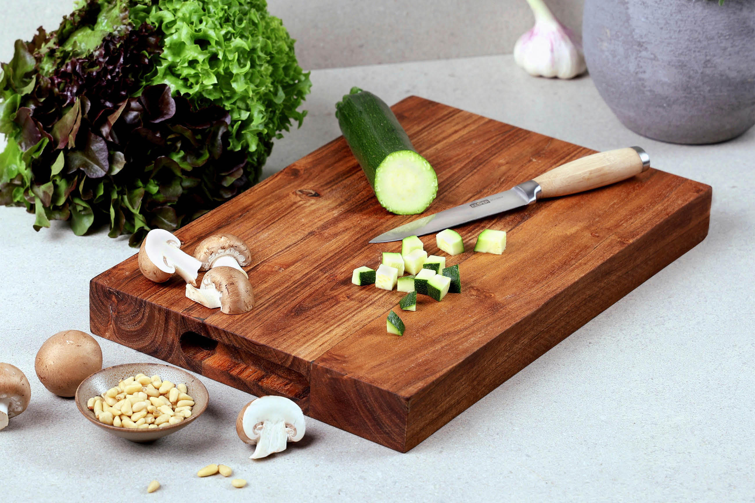 Ein Schneidebrett mit frischem Gemüse und einem scharfen Messer darauf.
