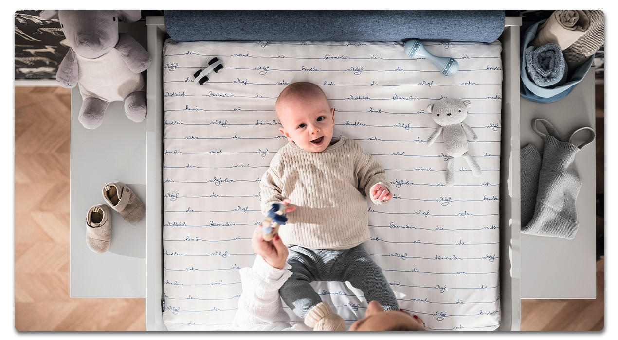 baby liegt auf der blauen Wickelkommode und lacht 