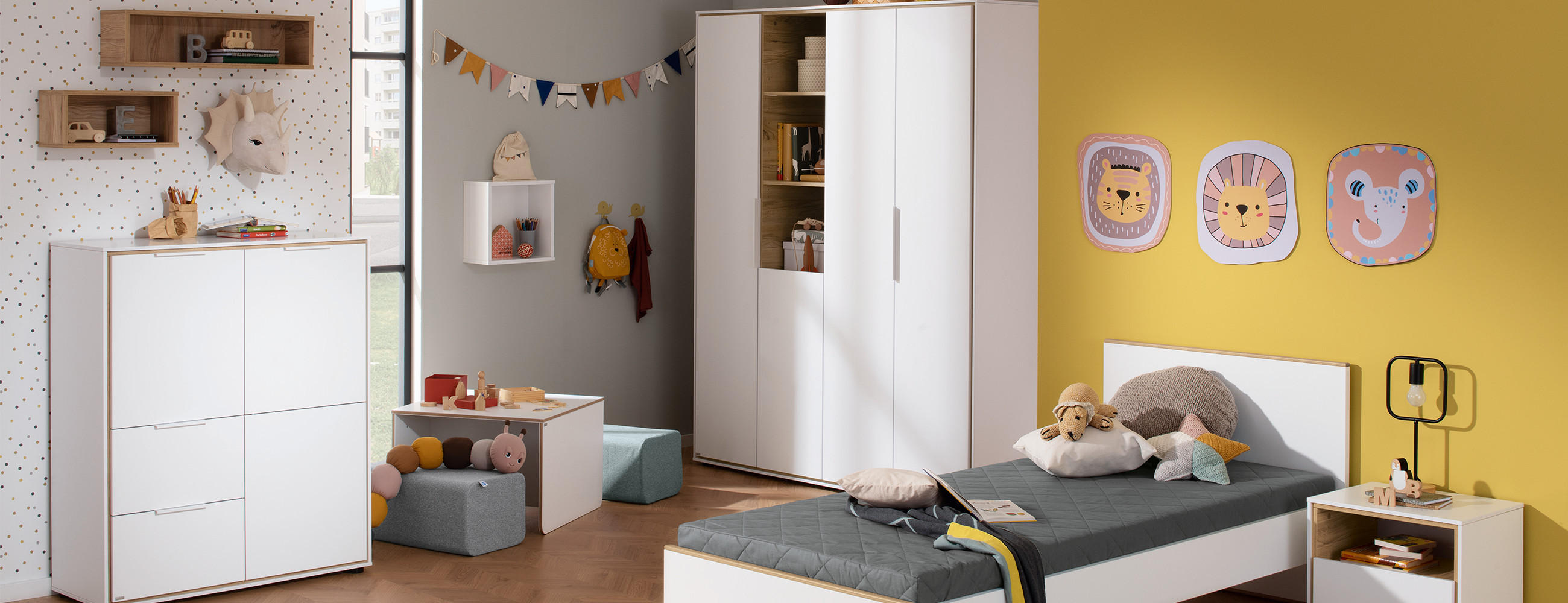 Kinderzimmer mit gelber Wand, weißem Bett, Schrank, Kommode, Regalen und Tierbildern an der Wand.