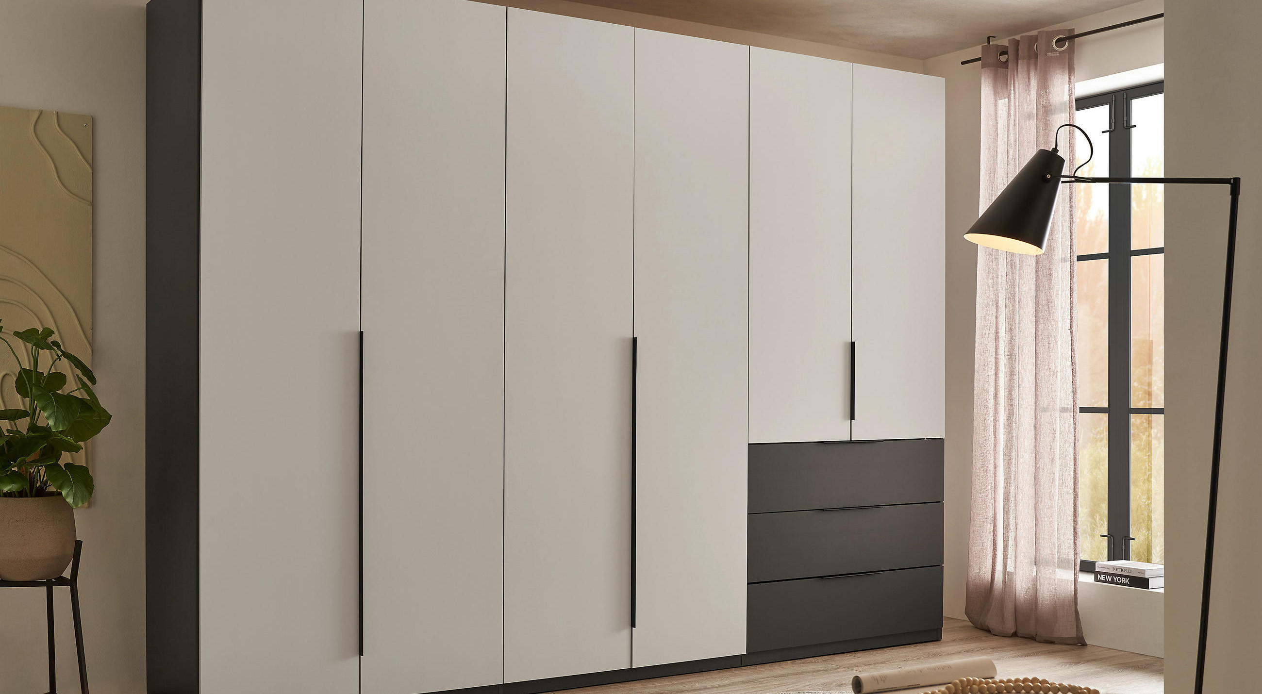 Kleiderschrank in beige mit dunkelgrauen Seitenwänden und Schubladen mit schwarzer Lampe im Vordergrund.
