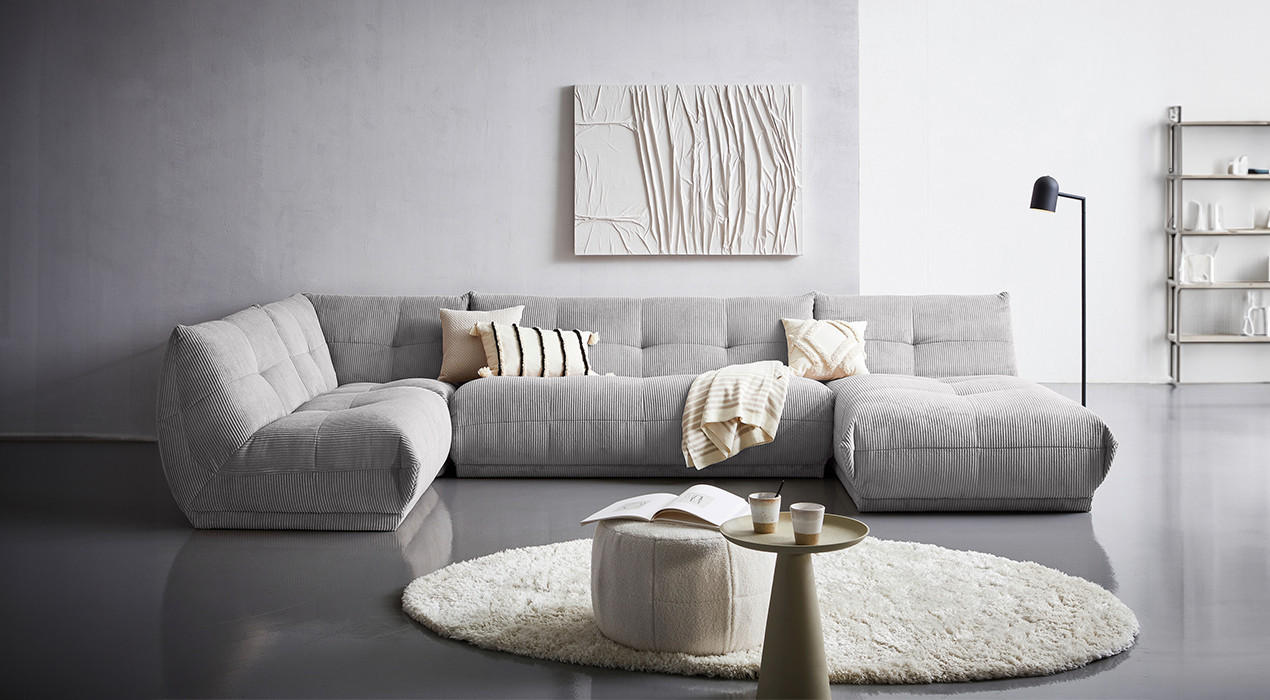Wohnzimmer in grau, graue Wohnlandschaft, graue Wandfarbe, beiger Teppich und Hocker, Bild