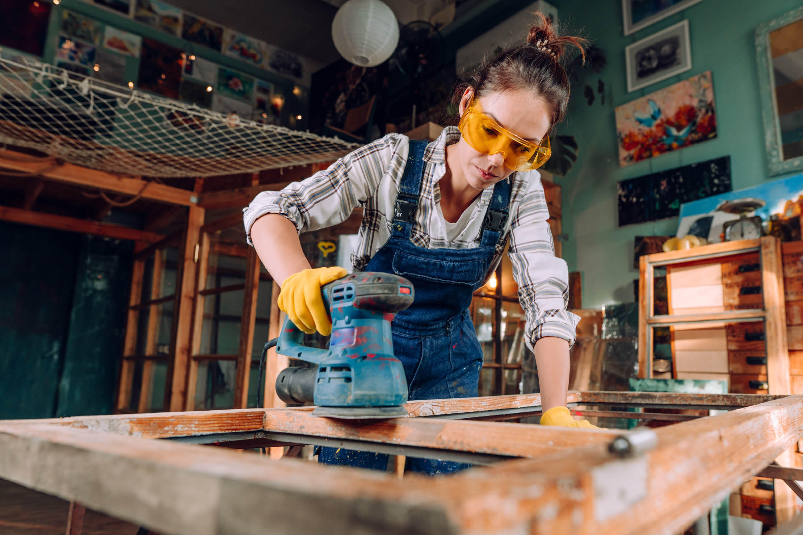 Person in Arbeitskleidung schleift Holzrahmen in Werkstatt.