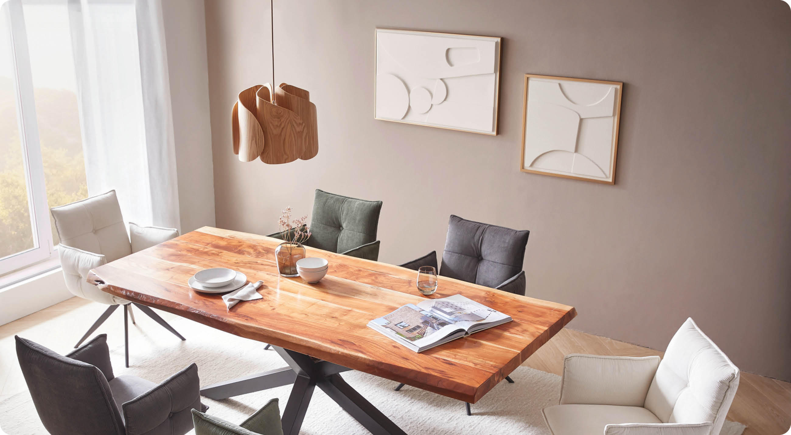 Esszimmer mit großem Holztisch, gemischten gepolsterten Stühlen und zwei minimalistischen Wandbildern auf beiger Wand