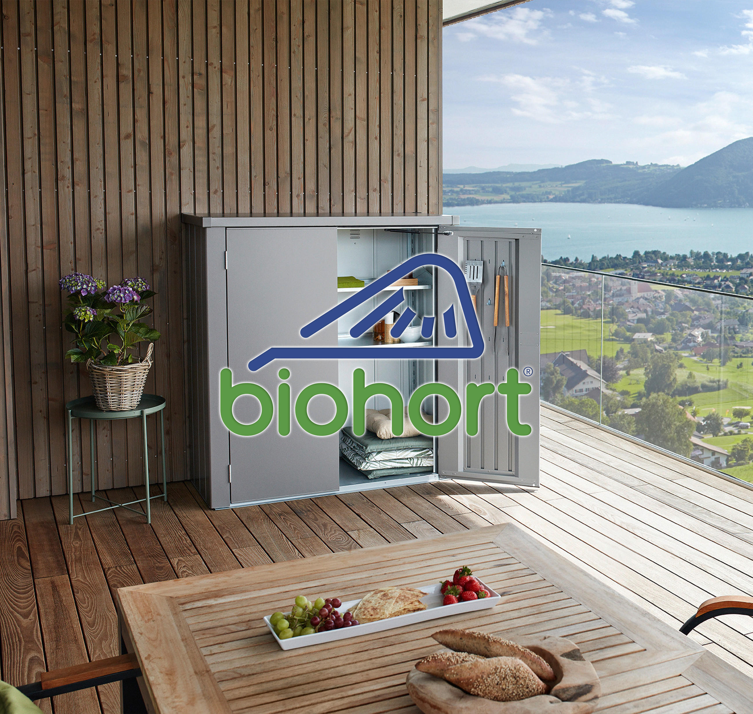 Balkon mit Blick auf einen See und Berge, ausgestattet mit einem Geräteschuppen der Marke Biohort.