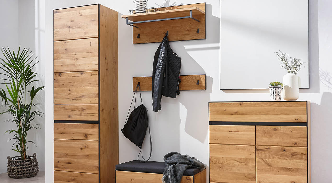 Moderner Flur mit Holzmöbeln, darunter ein hoher Schrank, eine Garderobe mit Jacken und Tasche sowie eine Kommode mit Spiegel und Pflanzen