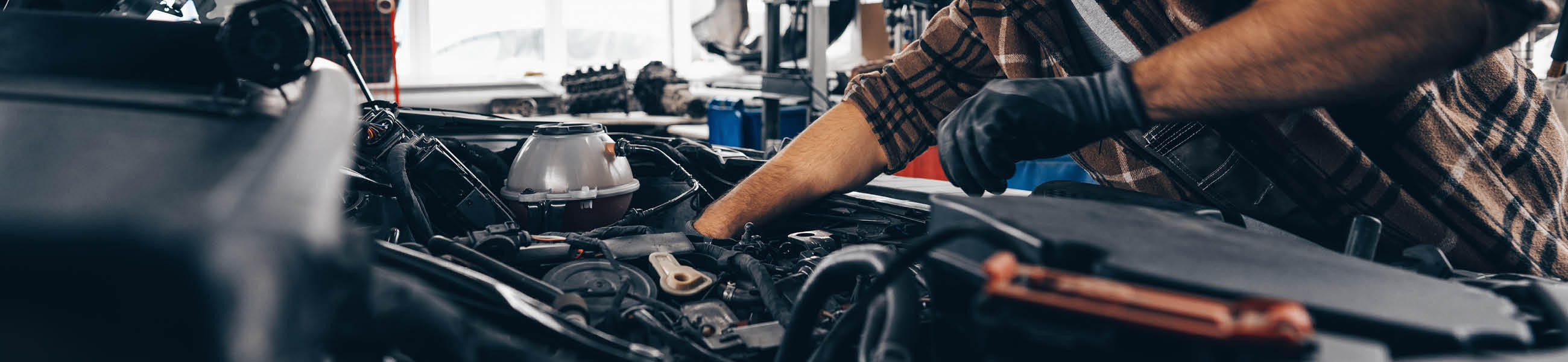 Mann in Handschuhen arbeitet an einem Motorraum, umgeben von Werkzeug und Maschinen, für einen Heimwerker-Ratgeber.