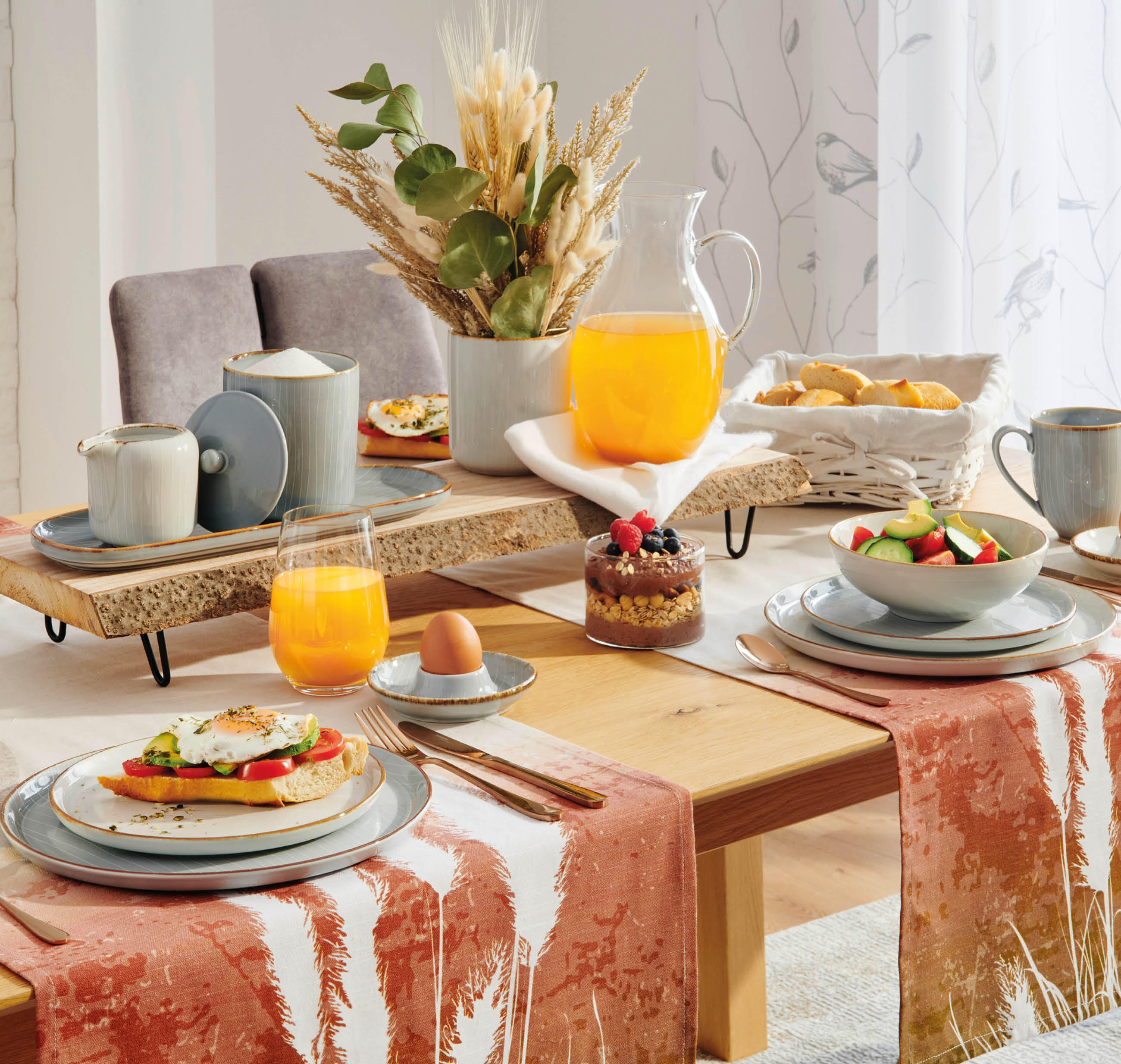 Esstisch mit gedeckten Tellern, Gläsern mit Orangensaft, Eiern in Eierbechern, Besteck und dekorativen Stoffläufern in warmen Farbtönen