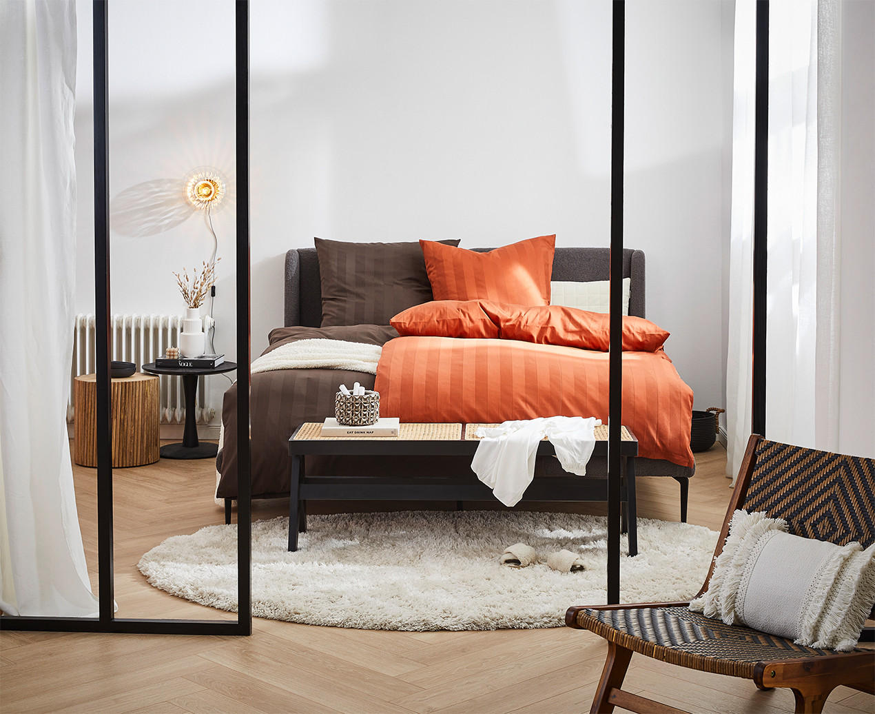 Modernes Schlafzimmer mit orange-brauner Bettwäsche, schwarzer Bank und dekorativen Akzenten.