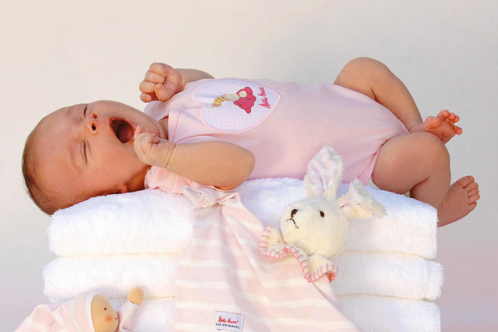 Ein Baby liegt entspannt auf einem bunten Stapel Handtücher.