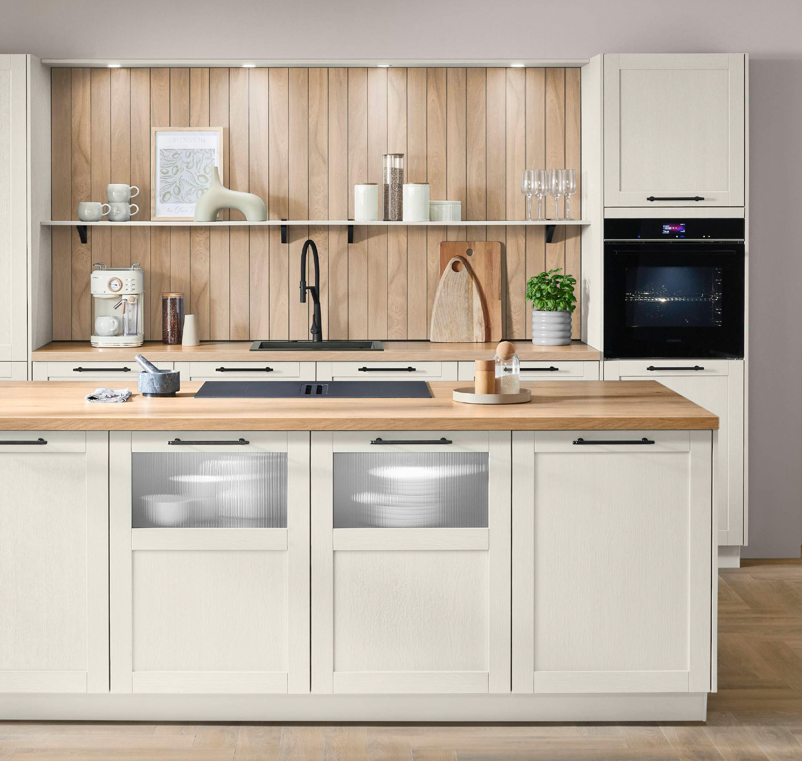 Helle Nobilia Markenküche im skandinavisch-modernen Stil: Cremeweiße Rahmenfronten und warme Holzarbeitsplatten, zentrale Kochinsel mit Kochfeld, Spülbereich in der Rückwand, offenes Regal, Einbauofen, große Fensterfront und heller Fischgrät-Parkettboden.