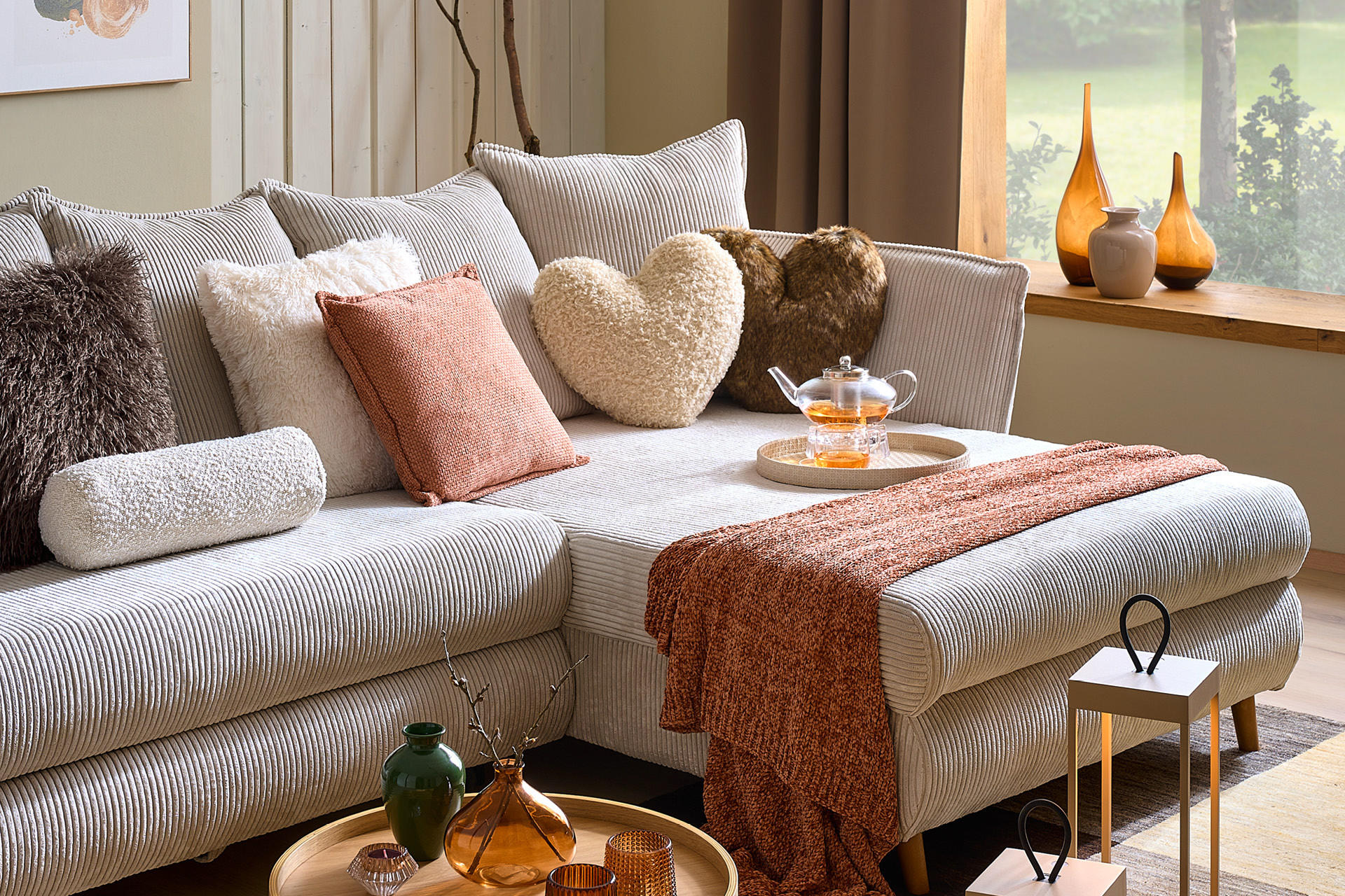 Hellgraues Sofa mit Wohntextilien in weiß und kastanienbraun