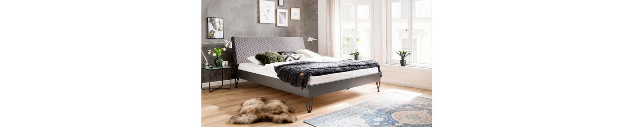 Graues Bett auf Metallfüßen mit Steppung im Kopftei.
