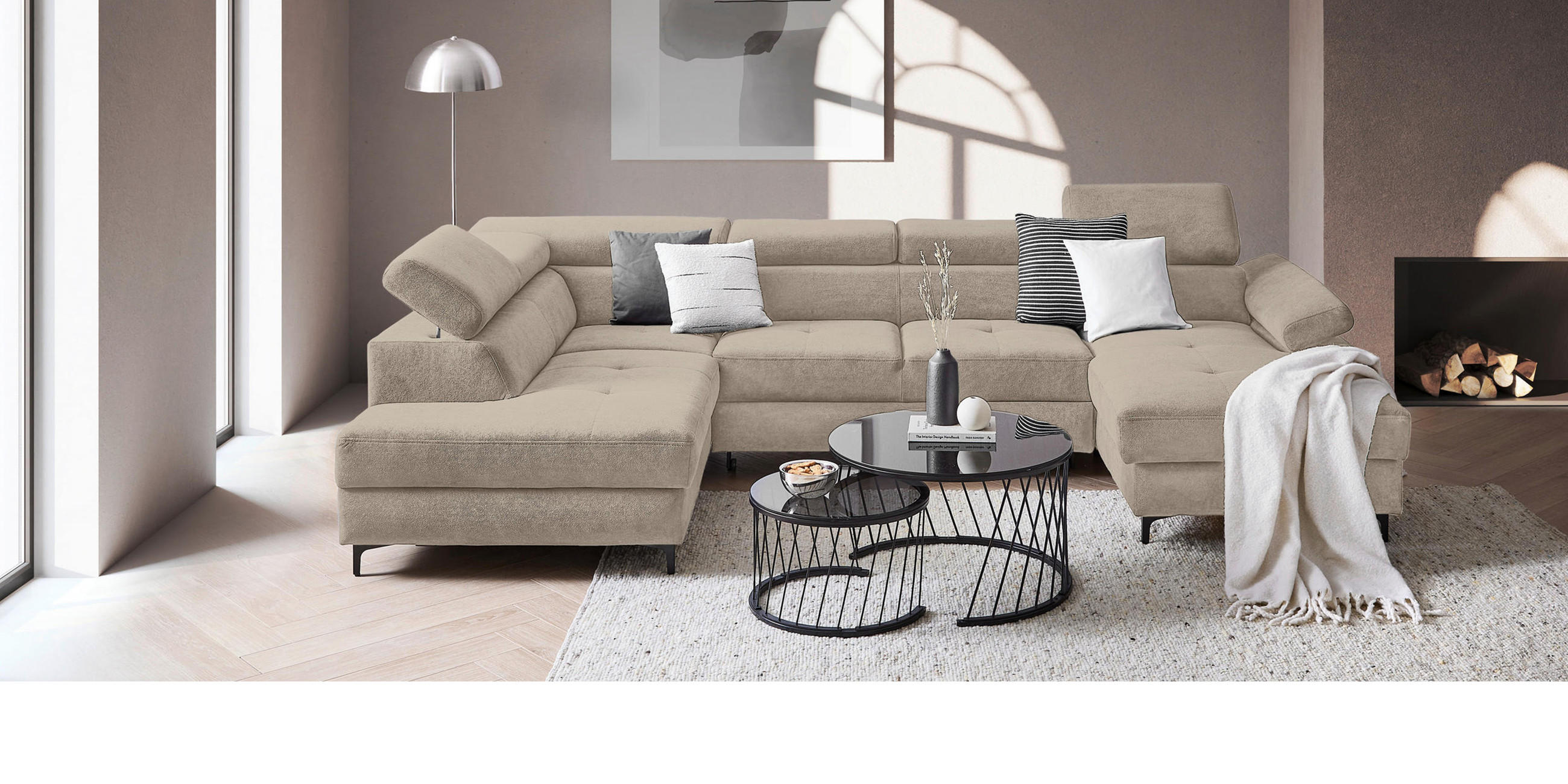 Beige Wohnlandschaft mit schwarzem Couchtisch vor altrosaner Wand mit Poster.