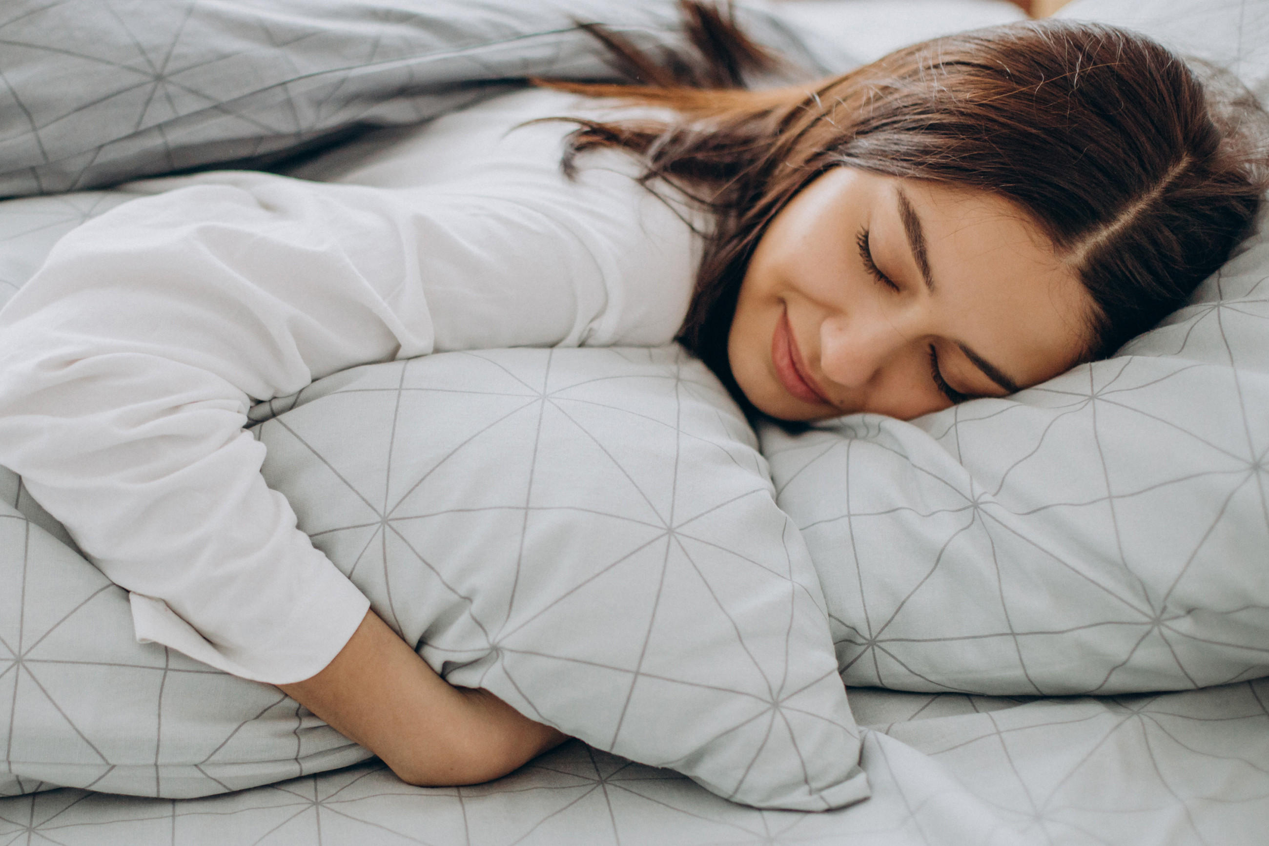 Eine Frau liegt entspannt auf einem Bett mit grauer Decke – Symbol für Abkühlung und Ruhe.