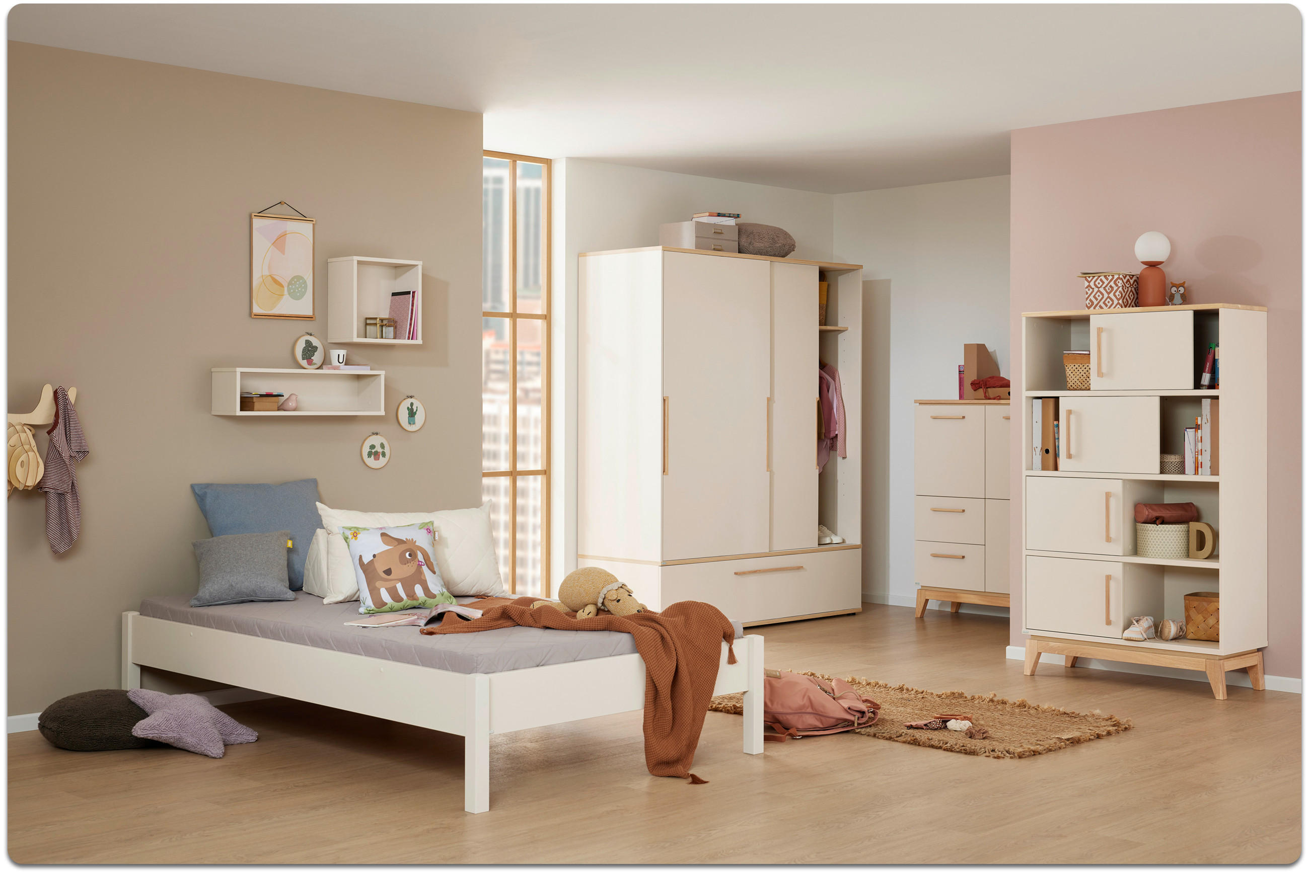 Kinderzimmer mit weißem Bett, Schrank, Regal und Kommode in hellem Holz, dekoriert mit Kissen, Decke und Spielzeug.