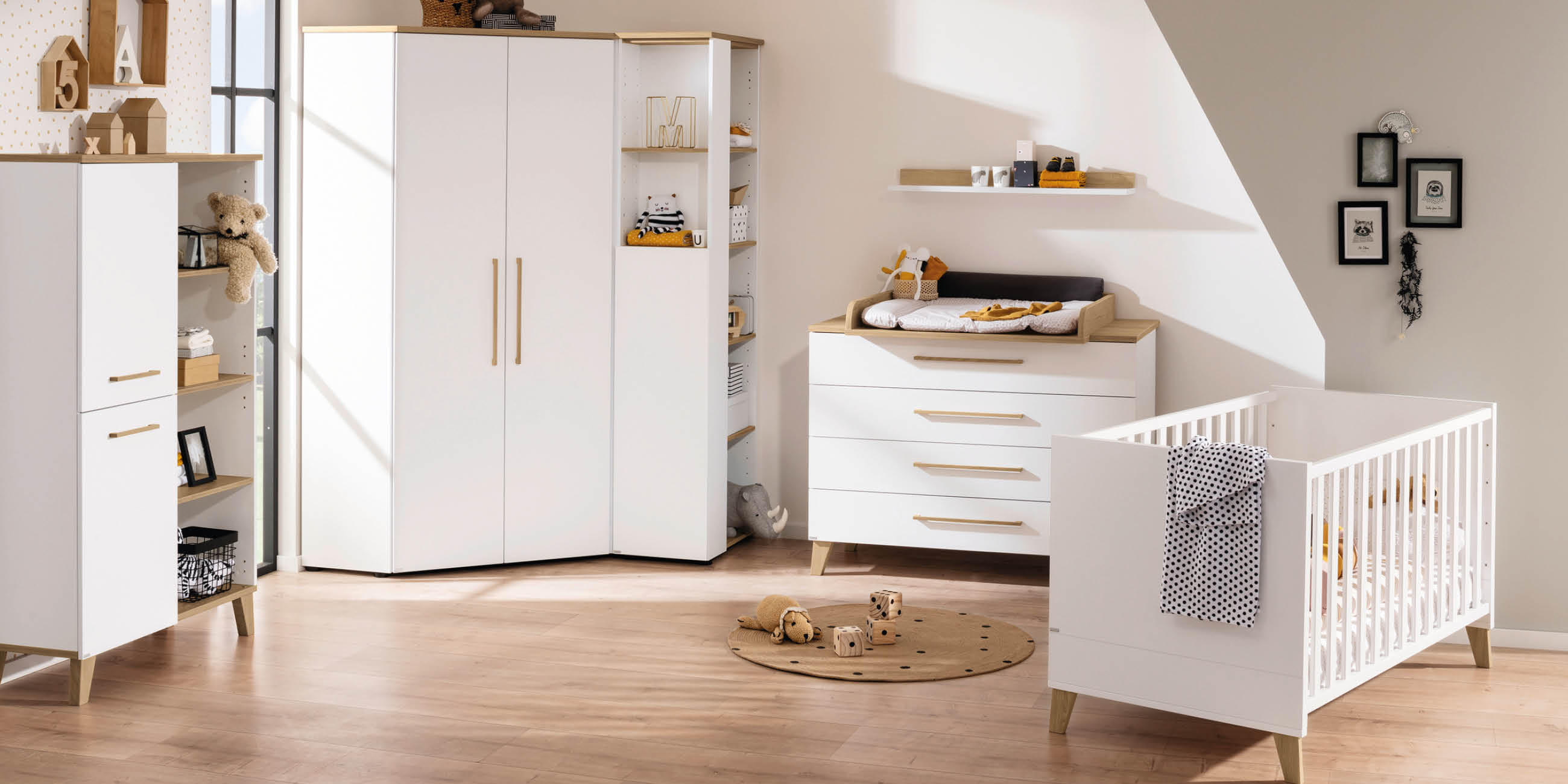 Modernes Babyzimmer mit weißen Möbeln, Holzakzenten, Spielzeug und dekorativen Elementen bei Tageslicht