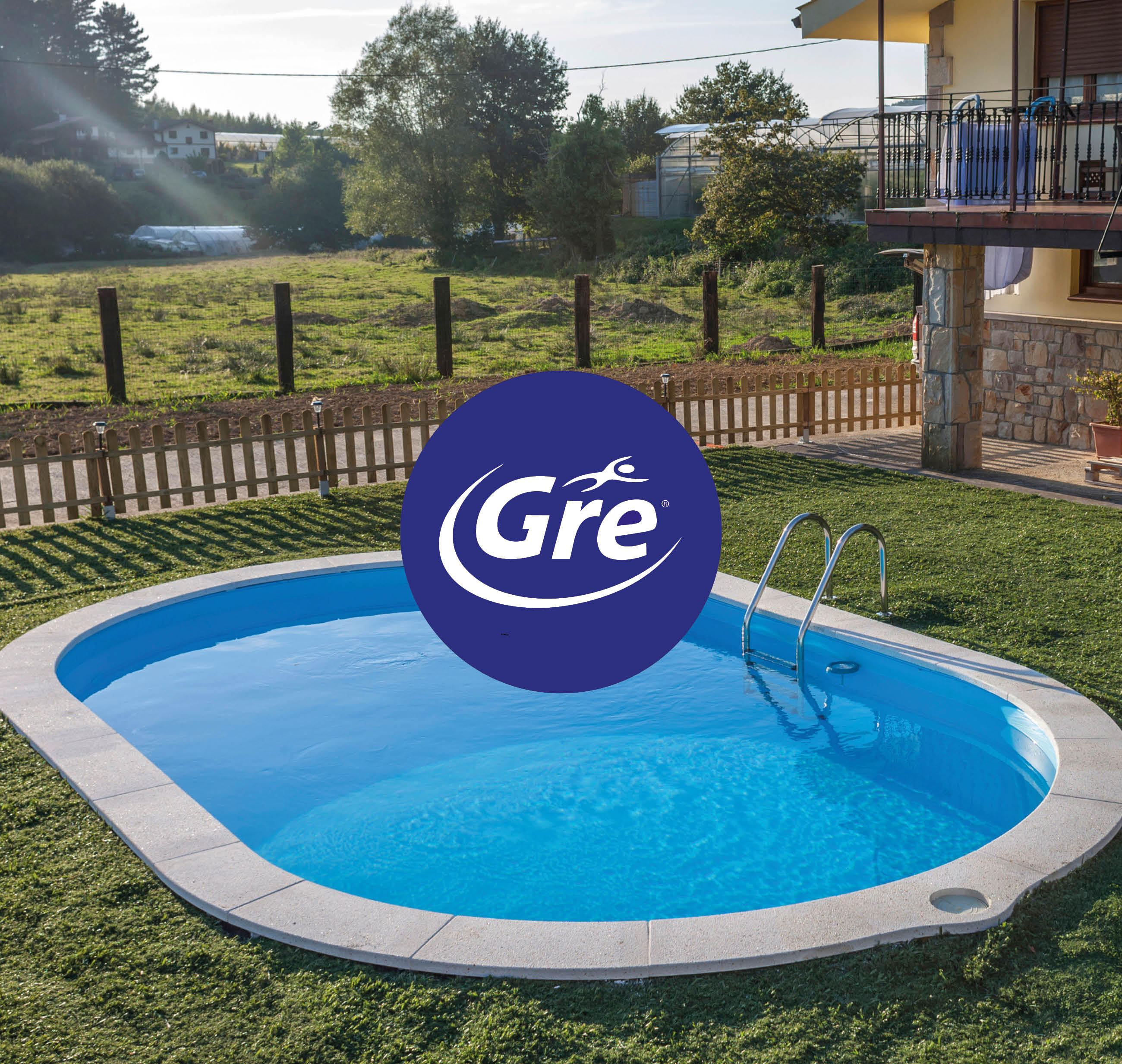 Ein ovaler Swimmingpool mit klarem Wasser, grauem Rand, Metallleiter und dem Logo „Gre“ in der Mitte, umgeben von grünem Rasen und einem Holzzaun im Hintergrund.