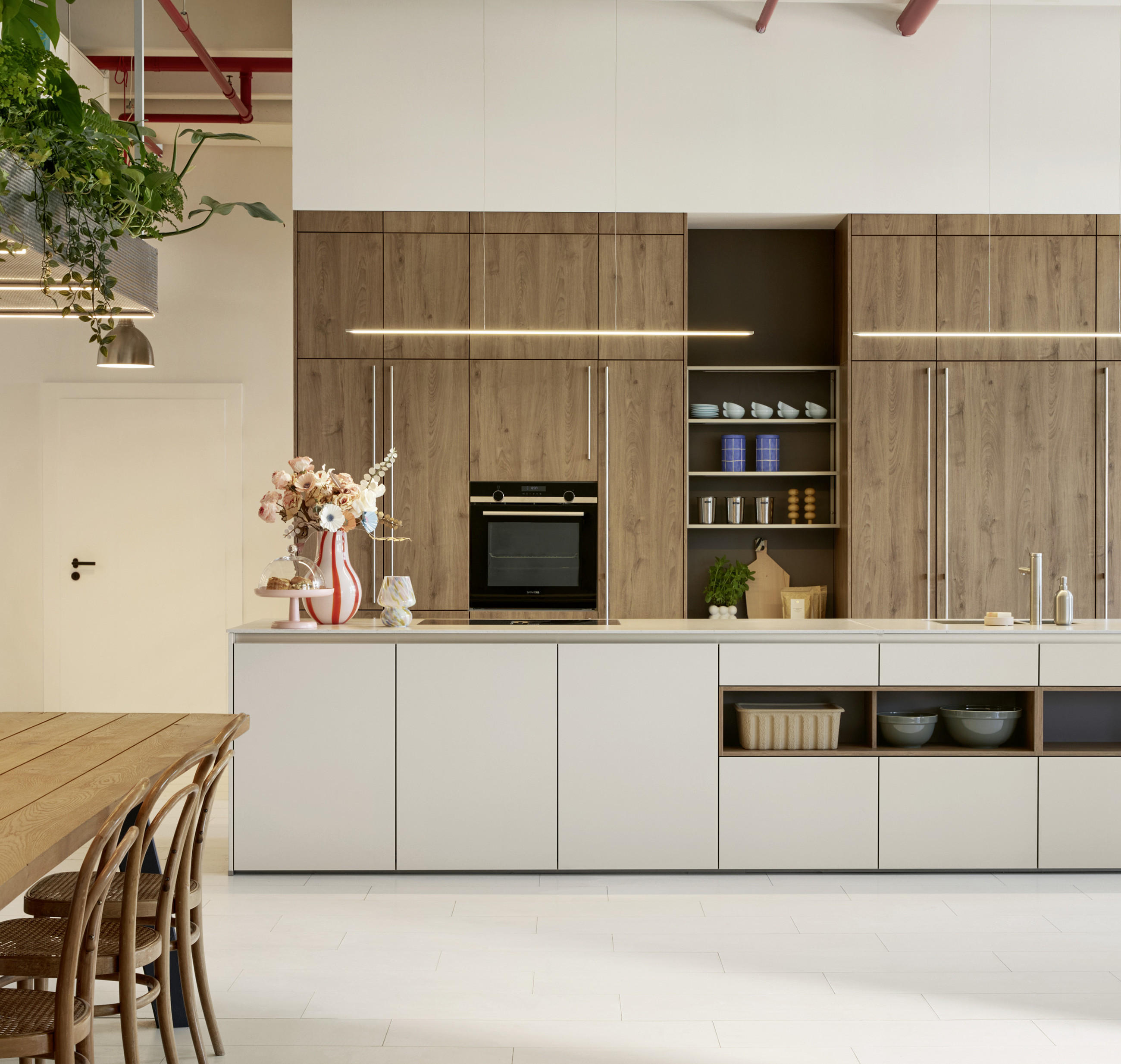 Trendige Küche in natürlichen Farben und modernen Küchengeräten, zusammen mit Esstisch aus Holz und stilvollen Regalen an der Wand.