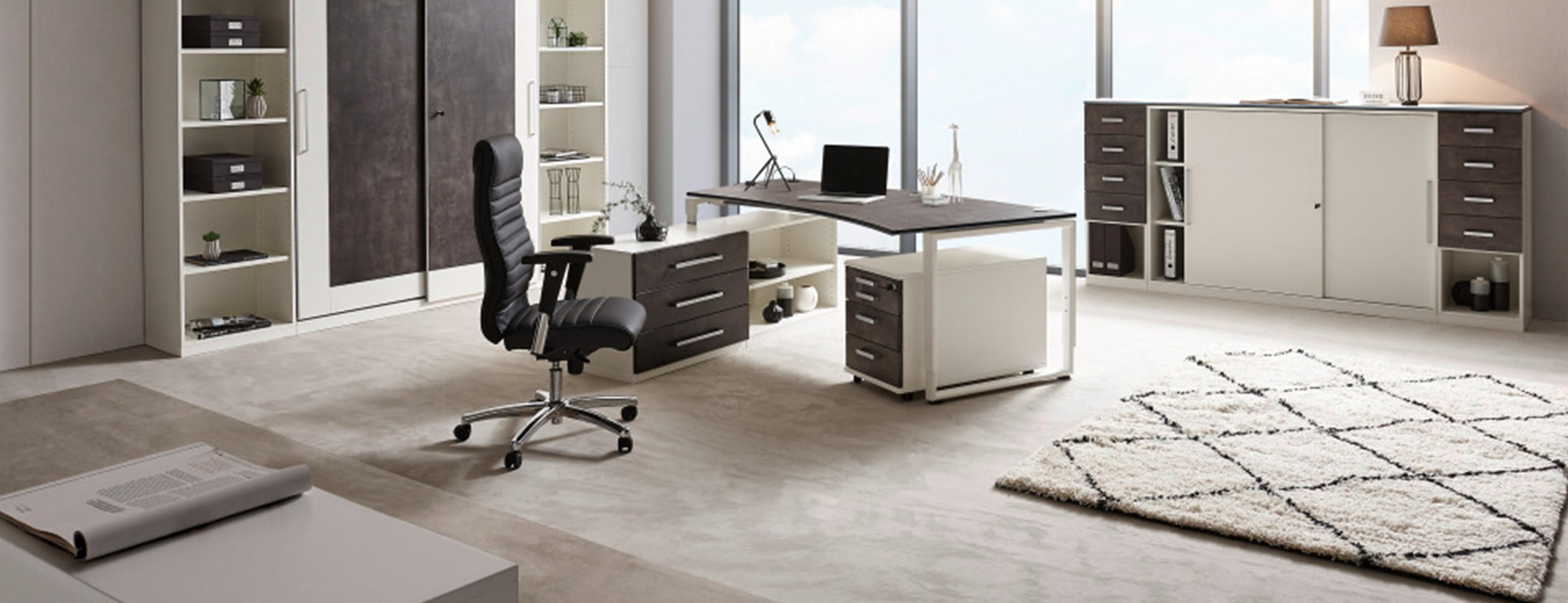 Modernes Büro mit großem Schreibtisch, schwarzem Bürostuhl, Regalen, Schränken, Weltkarte an der Wand und großen Fenstern mit Tageslicht.