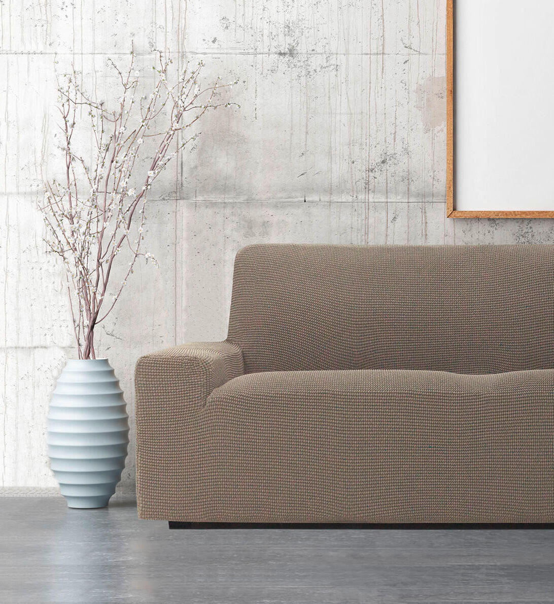 Predstavljeni so kavč s prevleko in vaza, ki sta umeščena pred steno, kar ustvarja prijetno vzdušje.