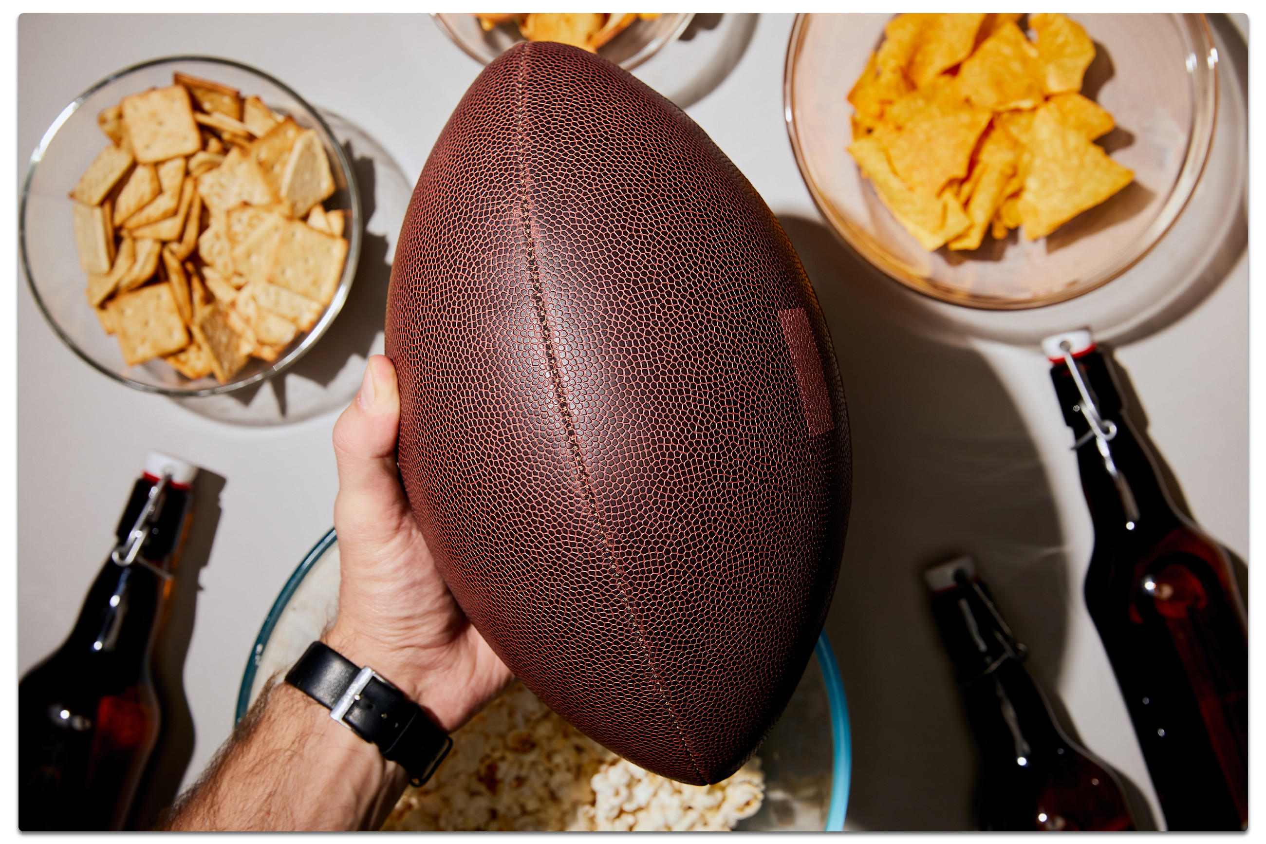 Eine Person hält einen Football neben einer Schüssel Chips und einem Bier, bereit für den Super Bowl.