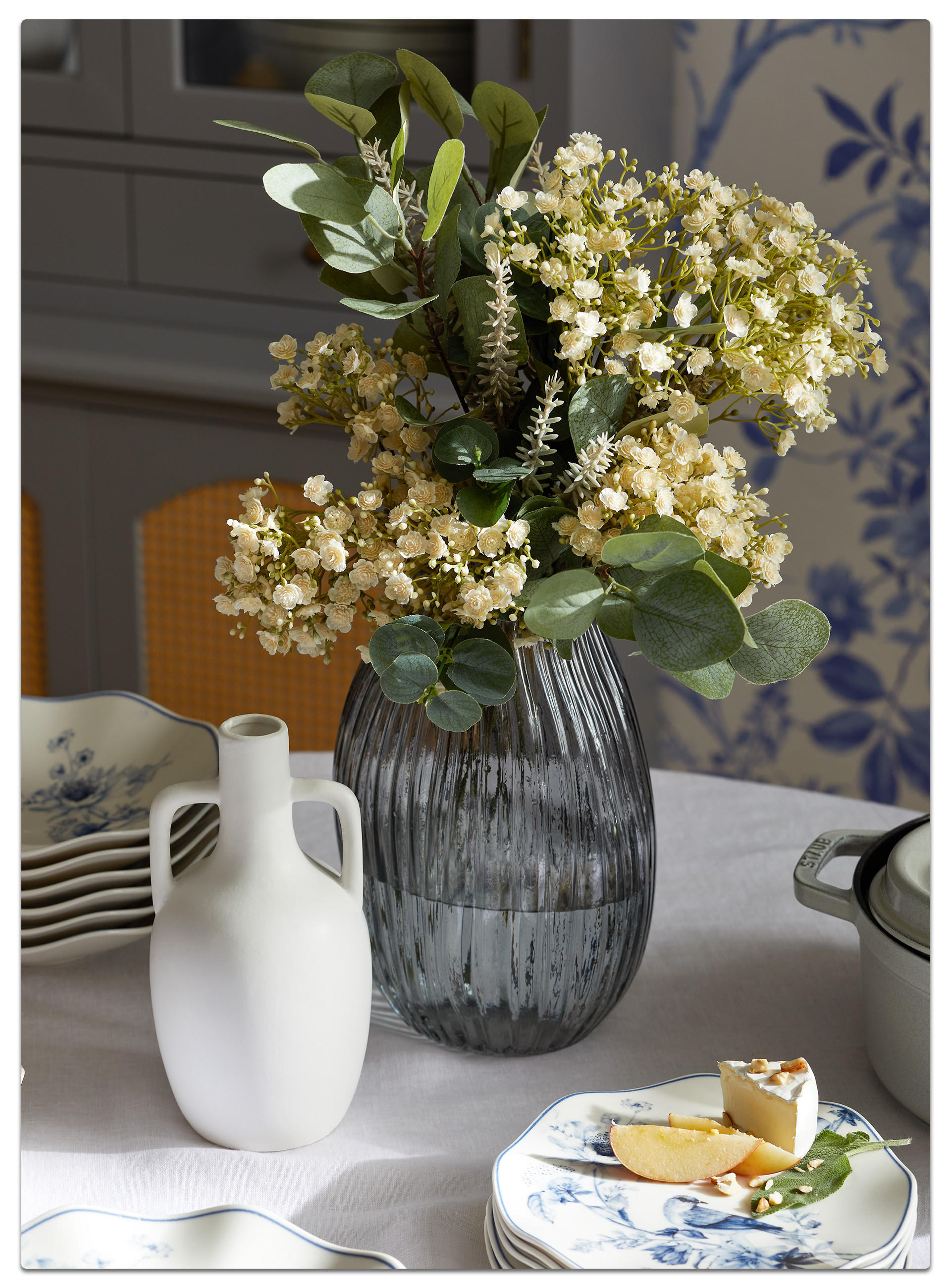 Eine Vase mit Blumen steht neben einem Teller mit Essen auf einem Tisch