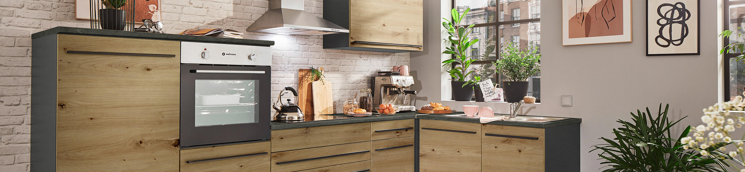  Moderne Küche mit Holzschränken und schwarzen Arbeitsflächen, weißer Backsteinwand, eingebautem Ofen, Kaffeemaschine und grünen Pflanzen als Dekoration.