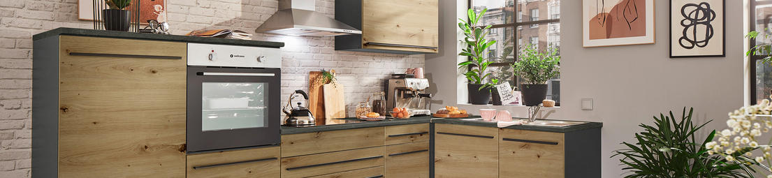  Moderne Küche mit Holzschränken und schwarzen Arbeitsflächen, weißer Backsteinwand, eingebautem Ofen, Kaffeemaschine und grünen Pflanzen als Dekoration.