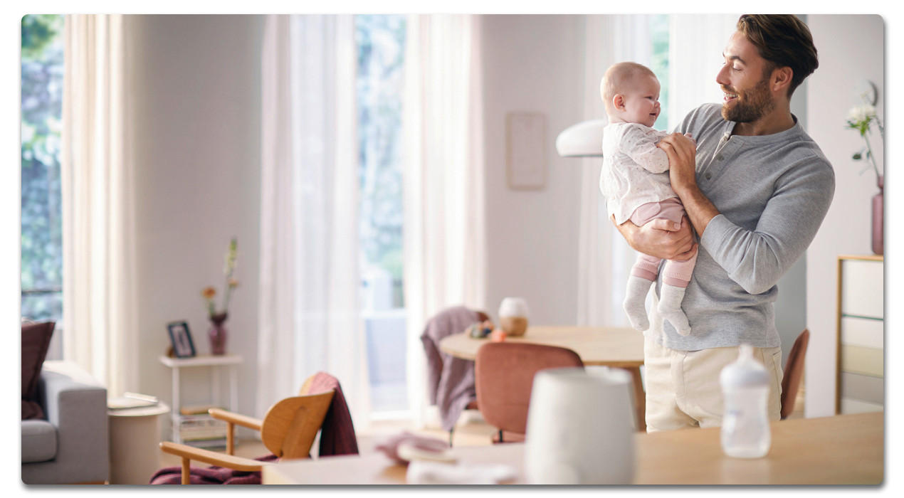 mann mit baby auf demarm und babyflasche auf dem tisch