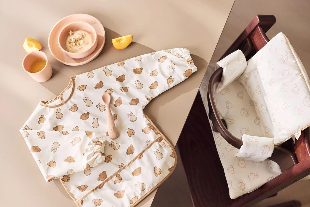 Otroški stol ob mizi, na kateri so slinček, žlica in krožnik za otroke