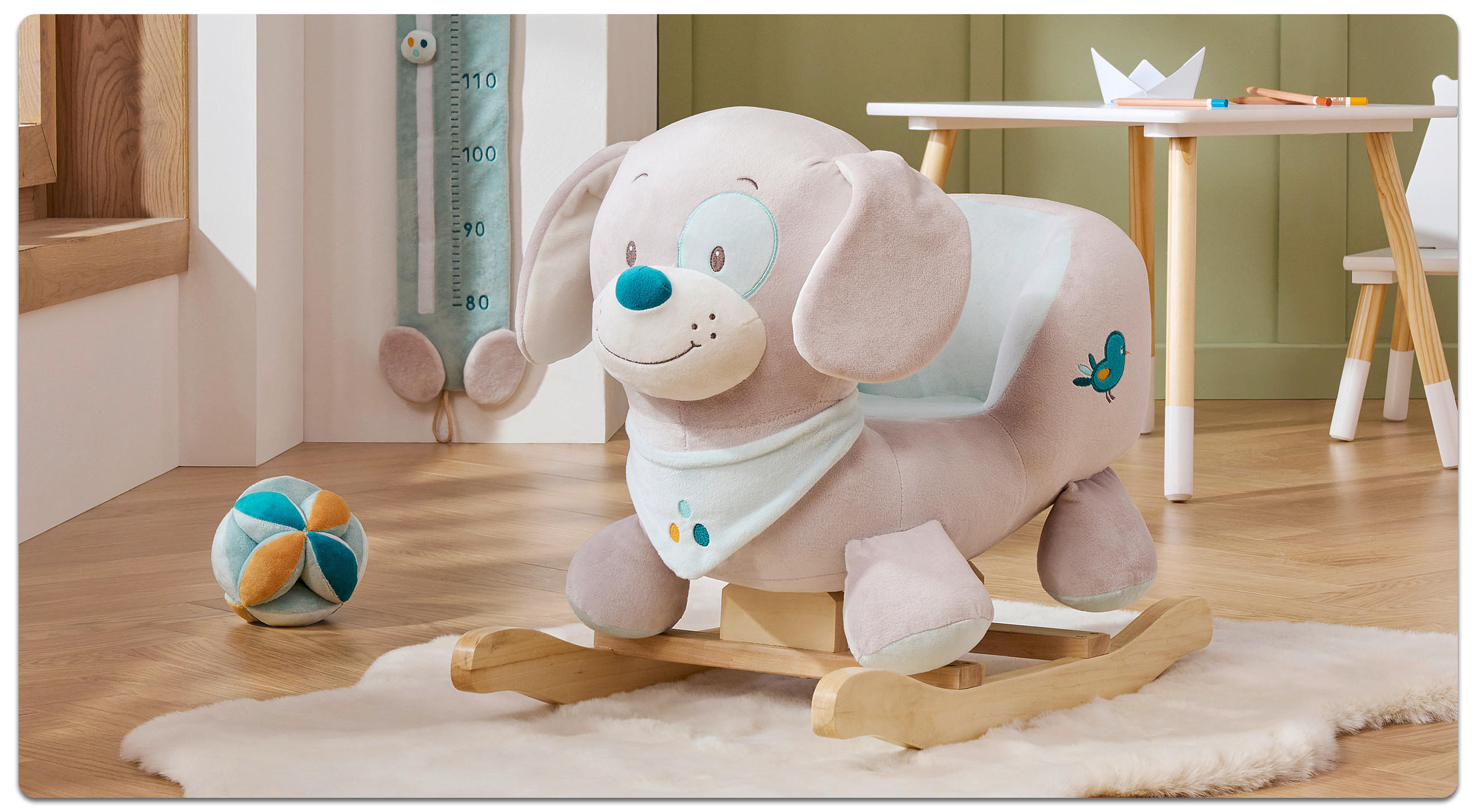 Spielball und Schaukeltier auf einem Fellteppich und Kinder-Tischgruppe im Hintergrund.