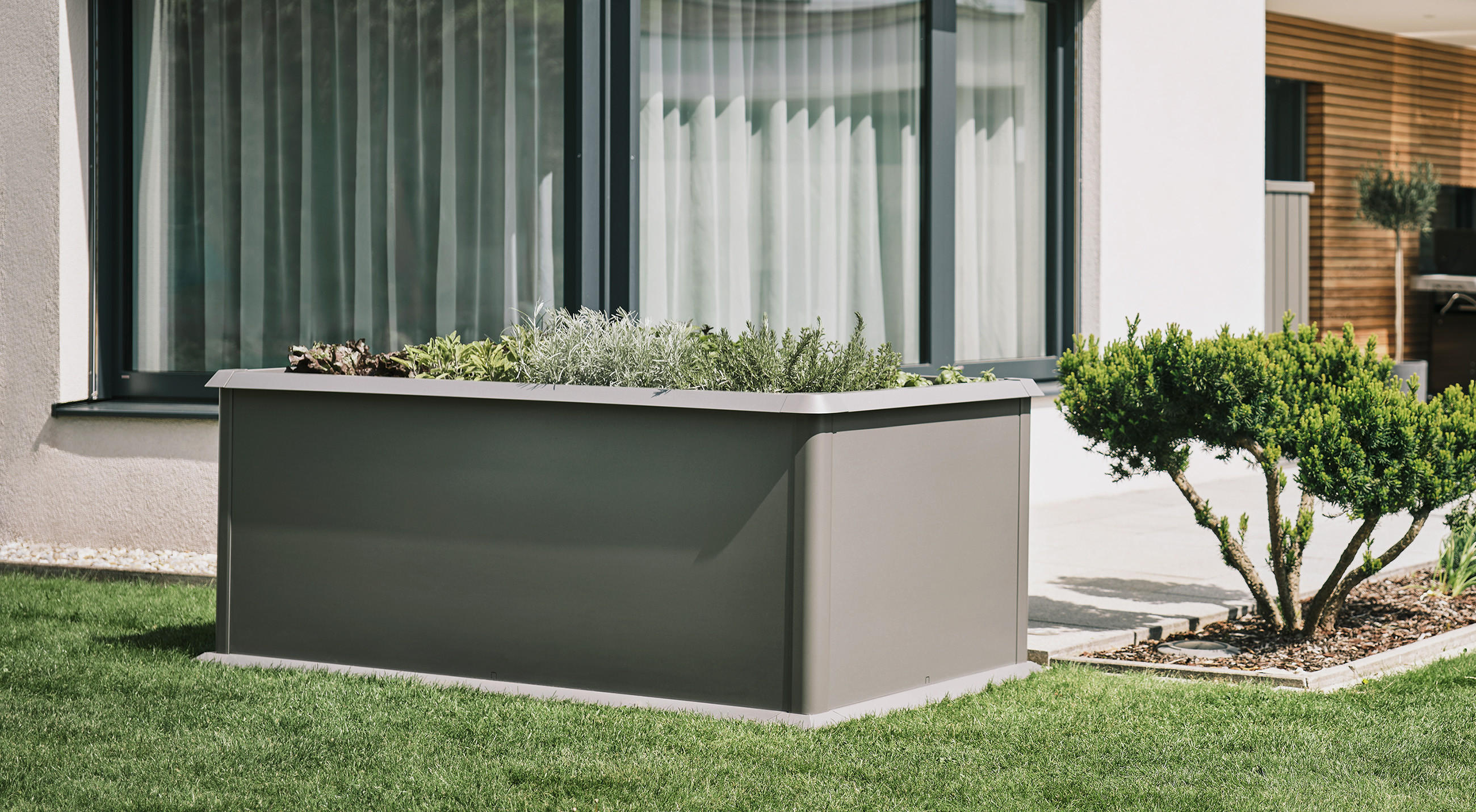 Hochbeet von LIEBHERR auf grüner Wiese vor modernem Haus.