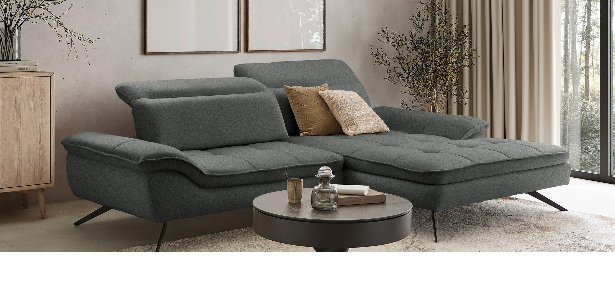 Ecksofa in dunkelgrau mit beigen Bildern an der Wand, beigen Vorhängen und dunklem Couchtisch.