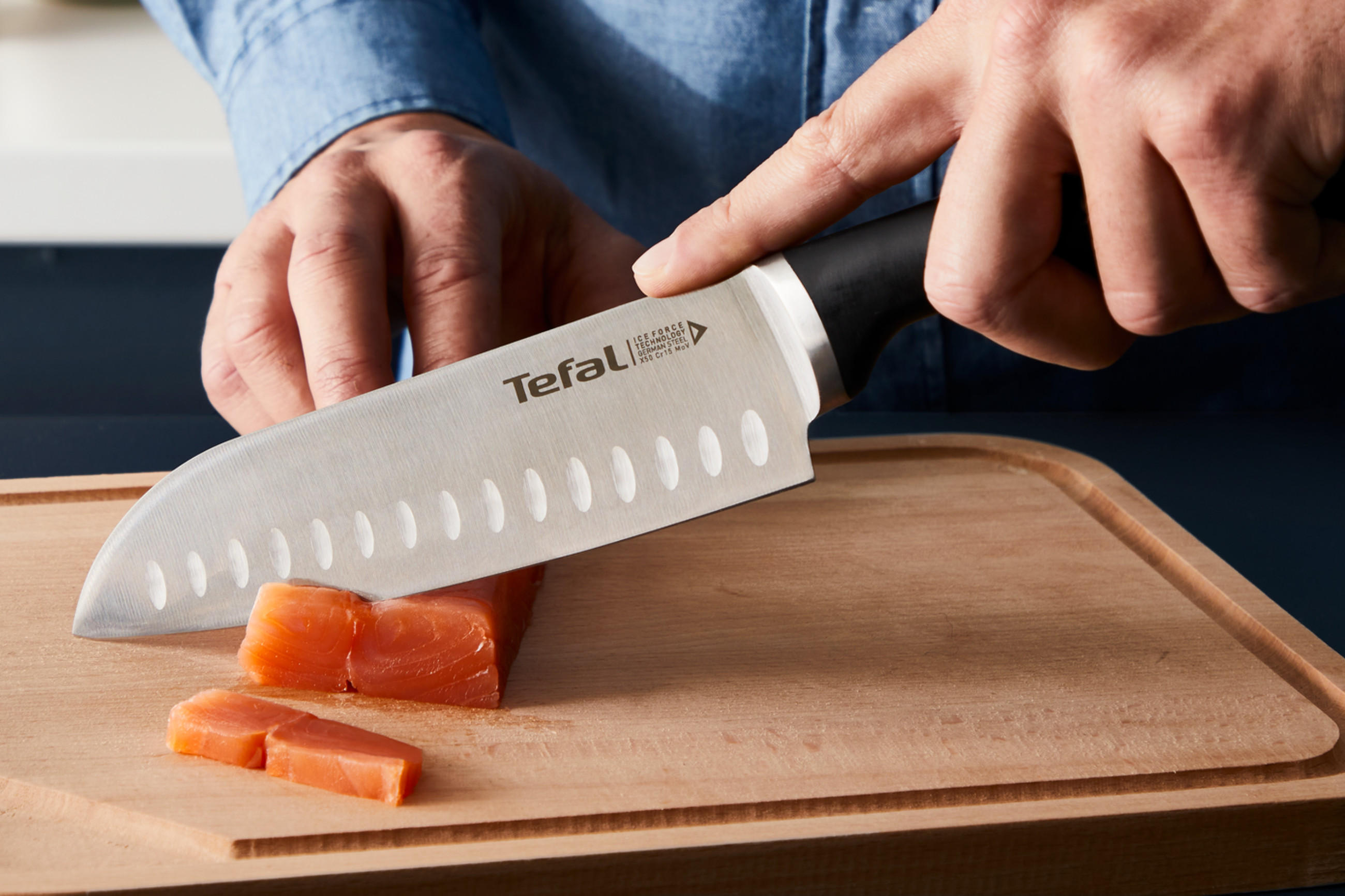 Nahaufnahme von TEFAL Küchenmesser beim Schneiden einer Karotte auf einem Holzschneidebrett.