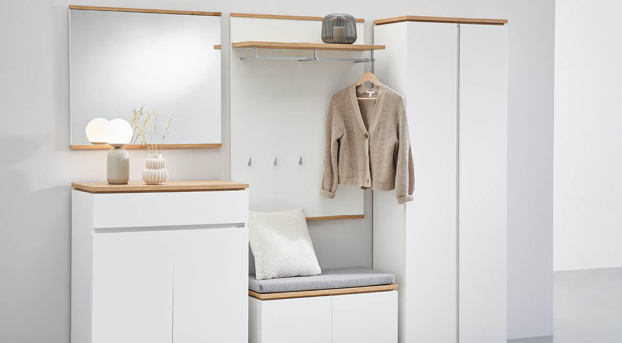 Moderner Flur mit weißen Möbeln und Holzakzenten, inklusive Spiegelschrank, Garderobe mit beigem Cardigan und Sitzbank mit Kissen