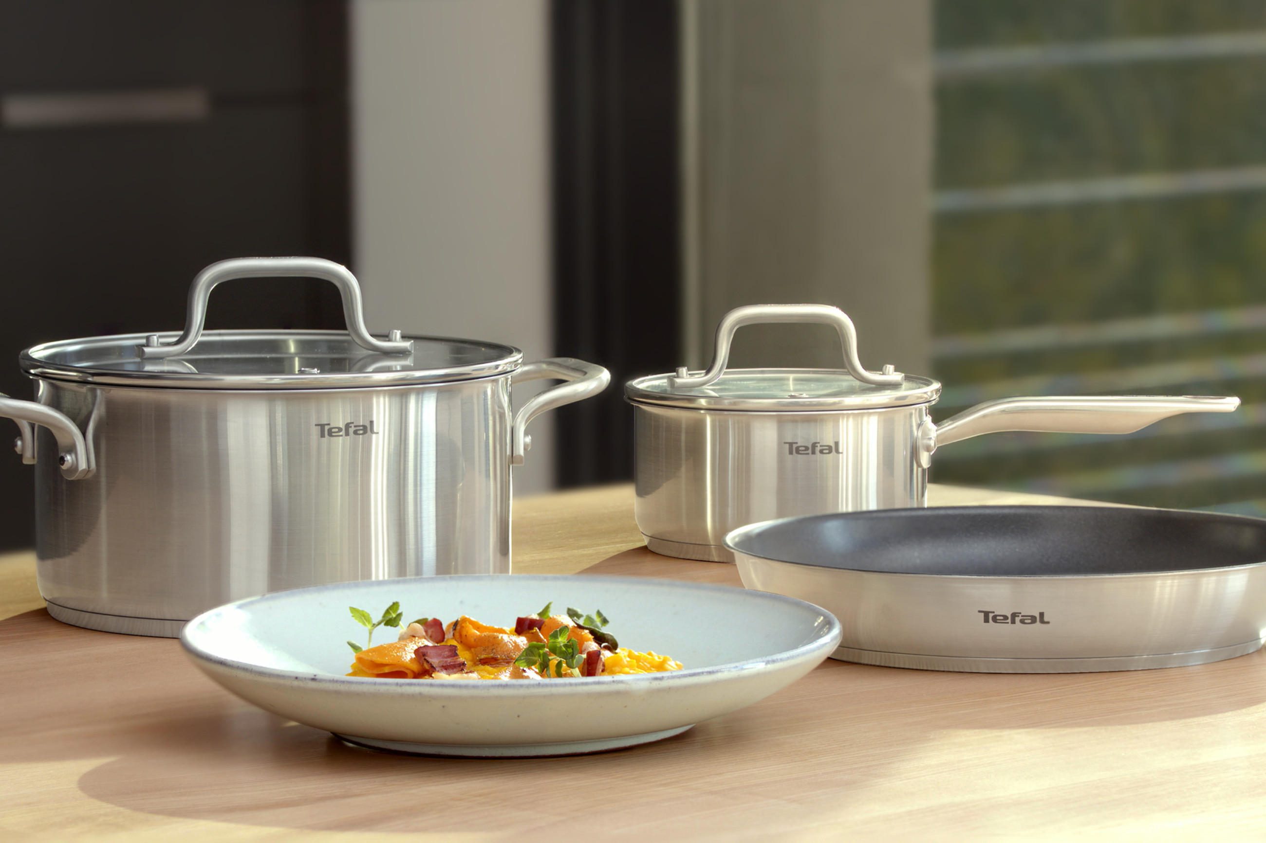 TEFAL Töpfe, Pfanne und Teller mit frisch angerichtetem Gericht auf einem Holztisch serviert.