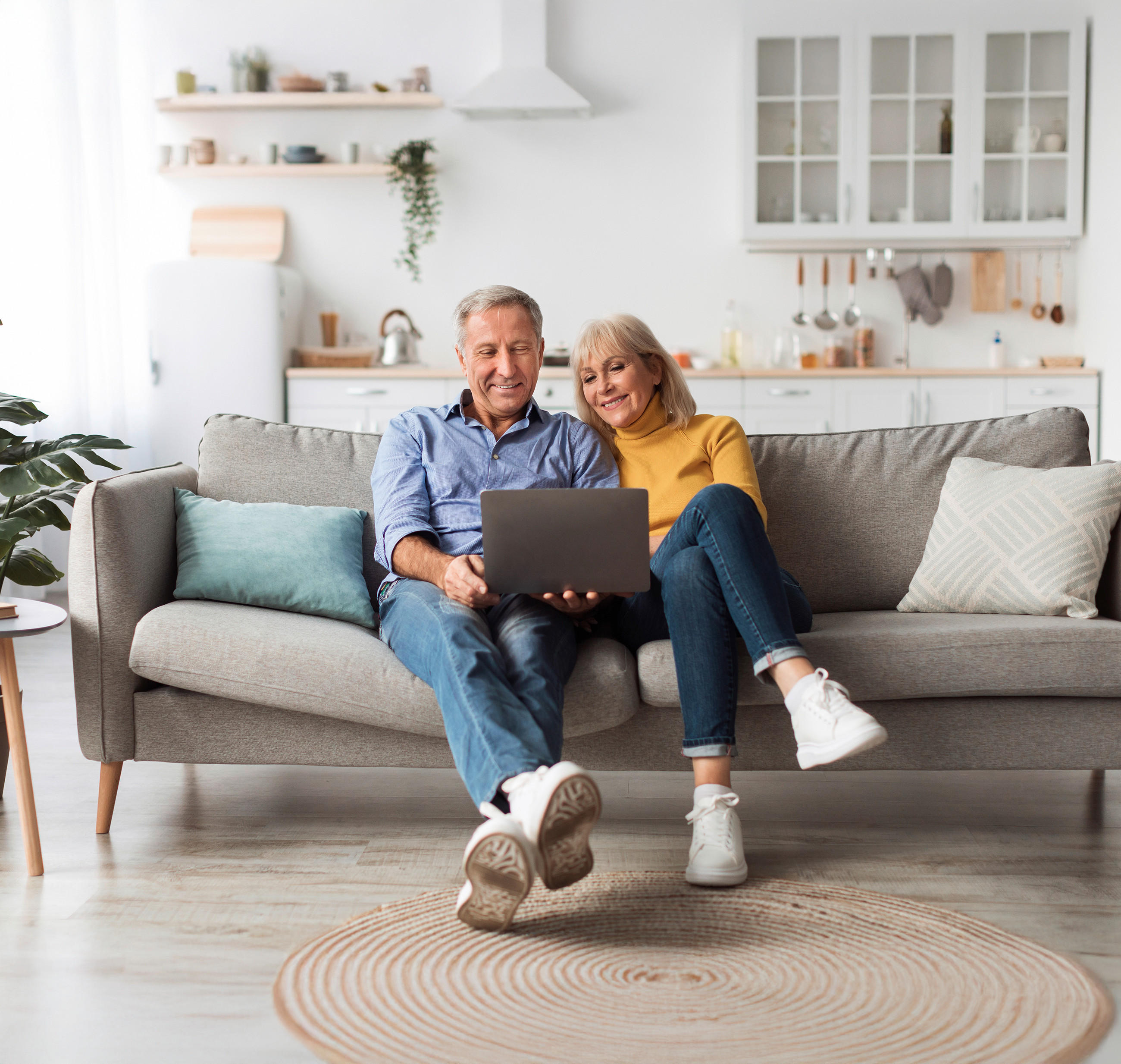 Ein Mann und eine Frau sitzen bequem Zuhause auf dem Sofa und planen ihre neue Küche online am Laptop. Im Hintergrund ist ihre aktuelle Küchenzeile zu erkennen.