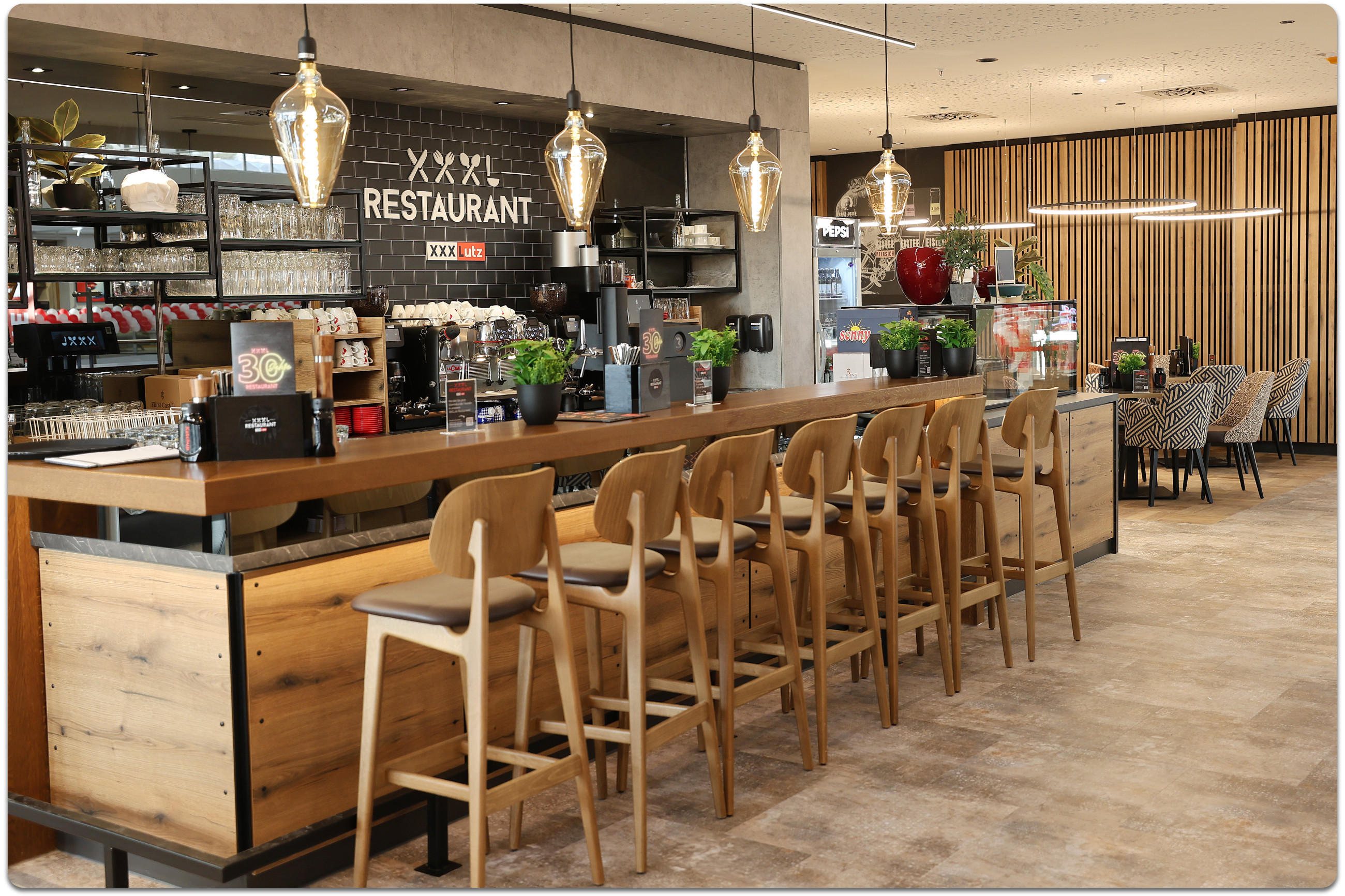 Theke aus Holz im Restaurant von XXXLutz Rangsdorf mit Barhockern aus Holz im Vordergrund und Esstisch-Nischen im Hintergrund.