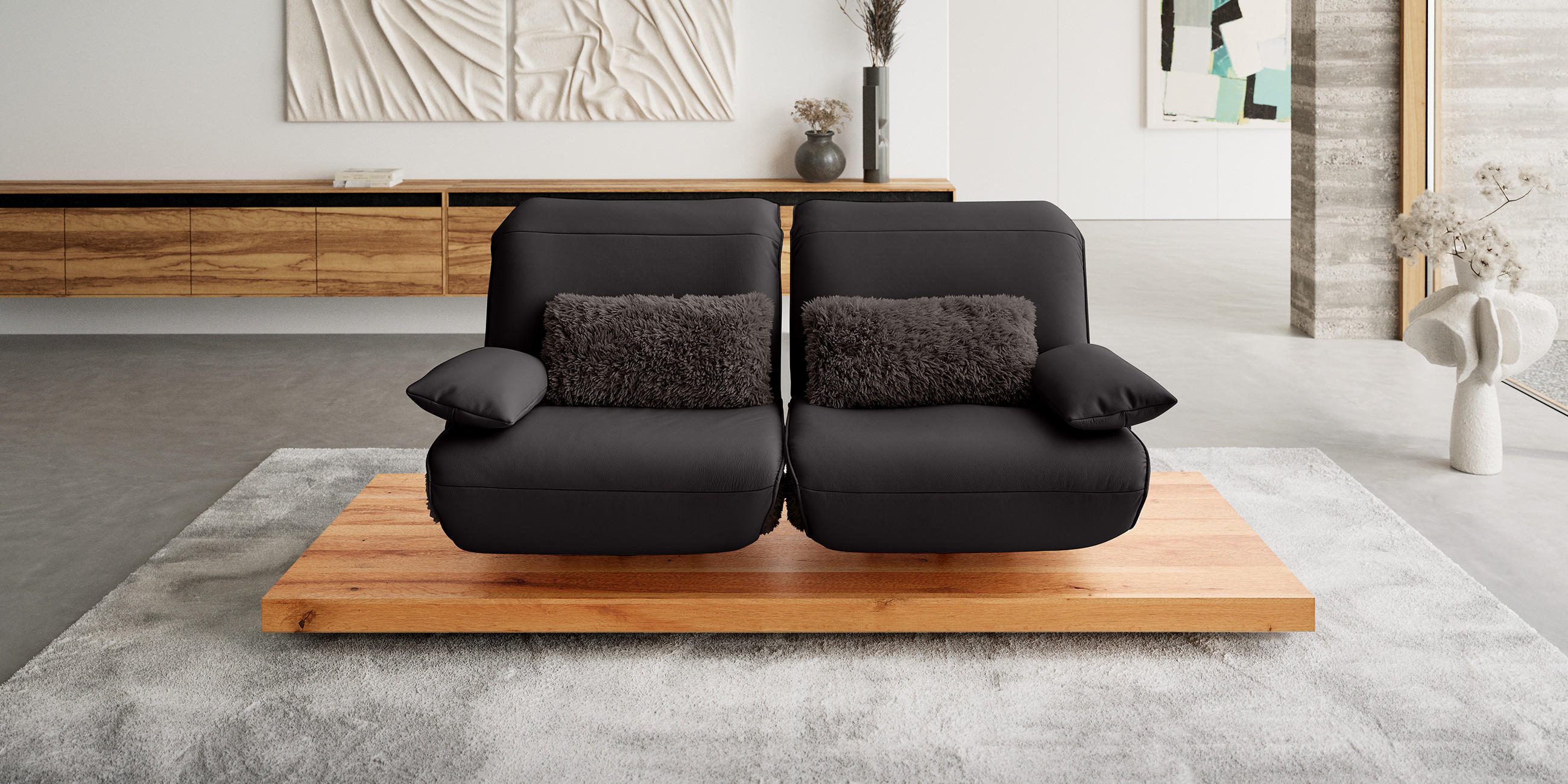 Koinor chwarzes Zweisitzer-Sofa mit Fellkissen auf Holzplattform in modernem Wohnzimmer.