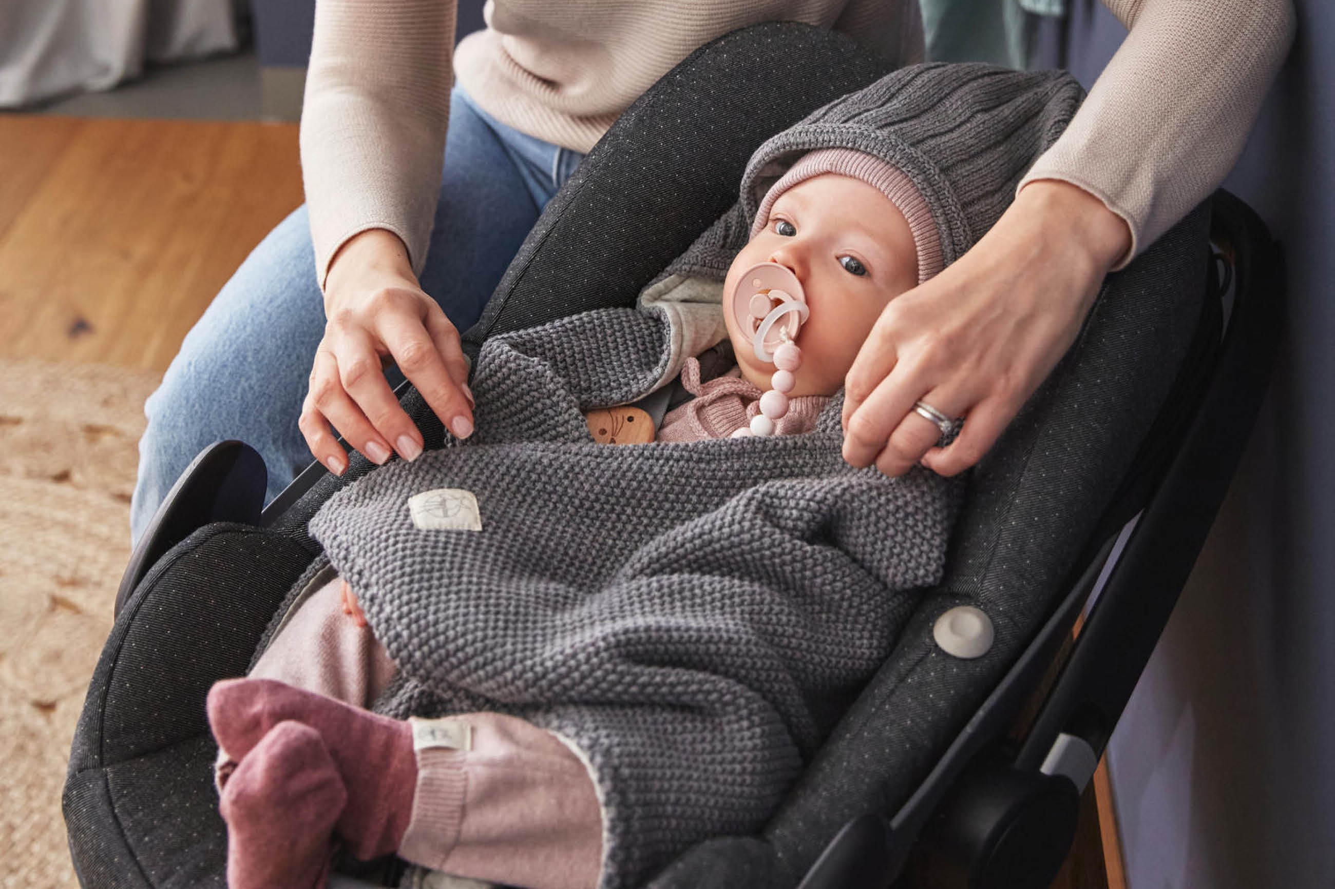 Eine Frau mit einem Baby im Autositz, das einen Schnuller von Lässig in den Mund hat.