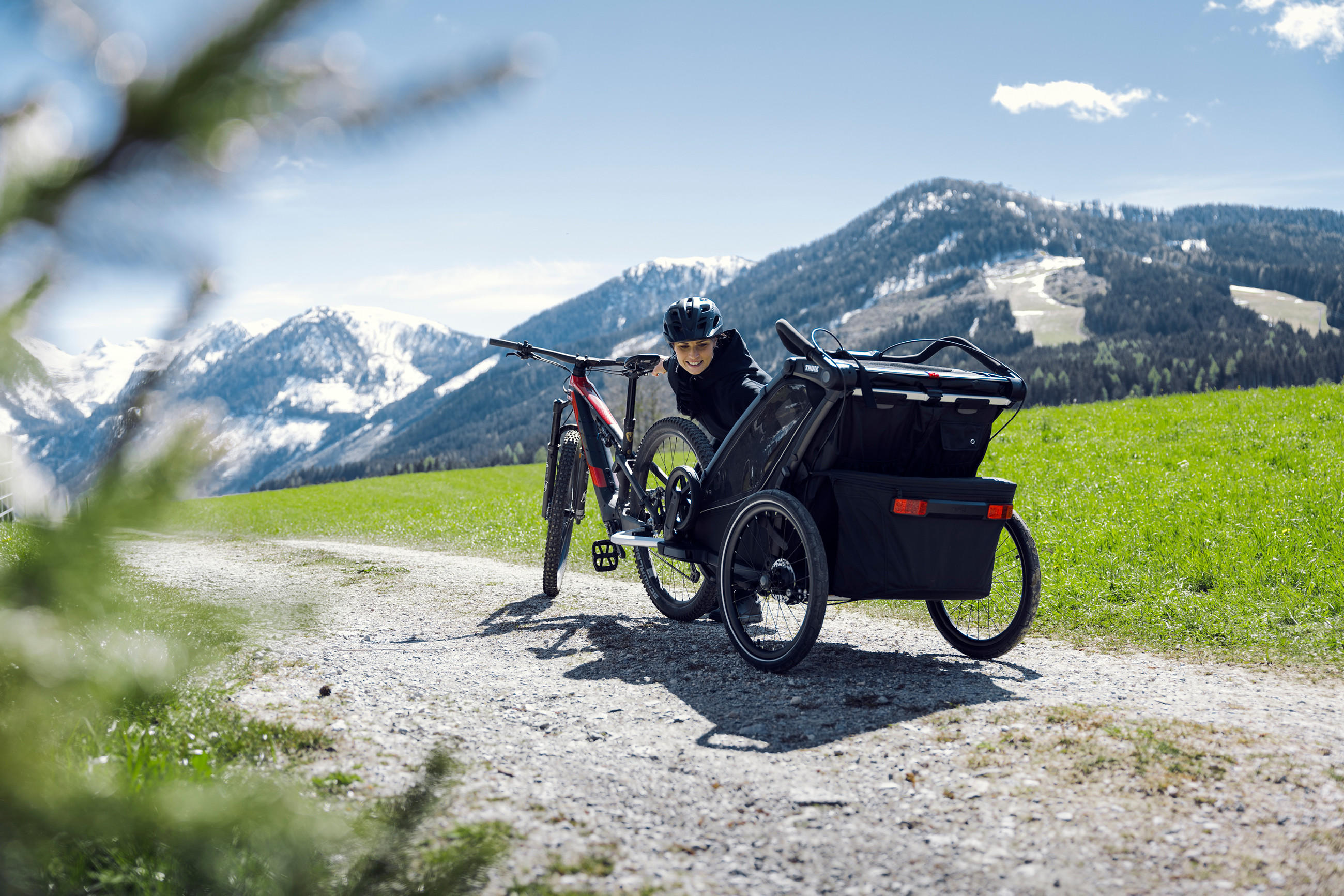 Schwarzes Fahrrad mit angehängtem Thule Kinderanhänger auf einem Weg in den Bergen bei Sonnenschein