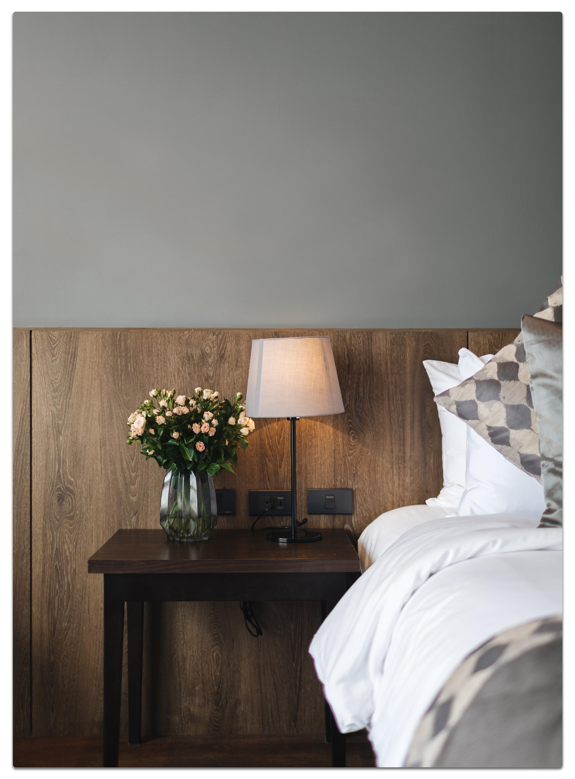Gemütliches Schlafzimmer mit weißer Bettwäsche, Blumen und Lampe.