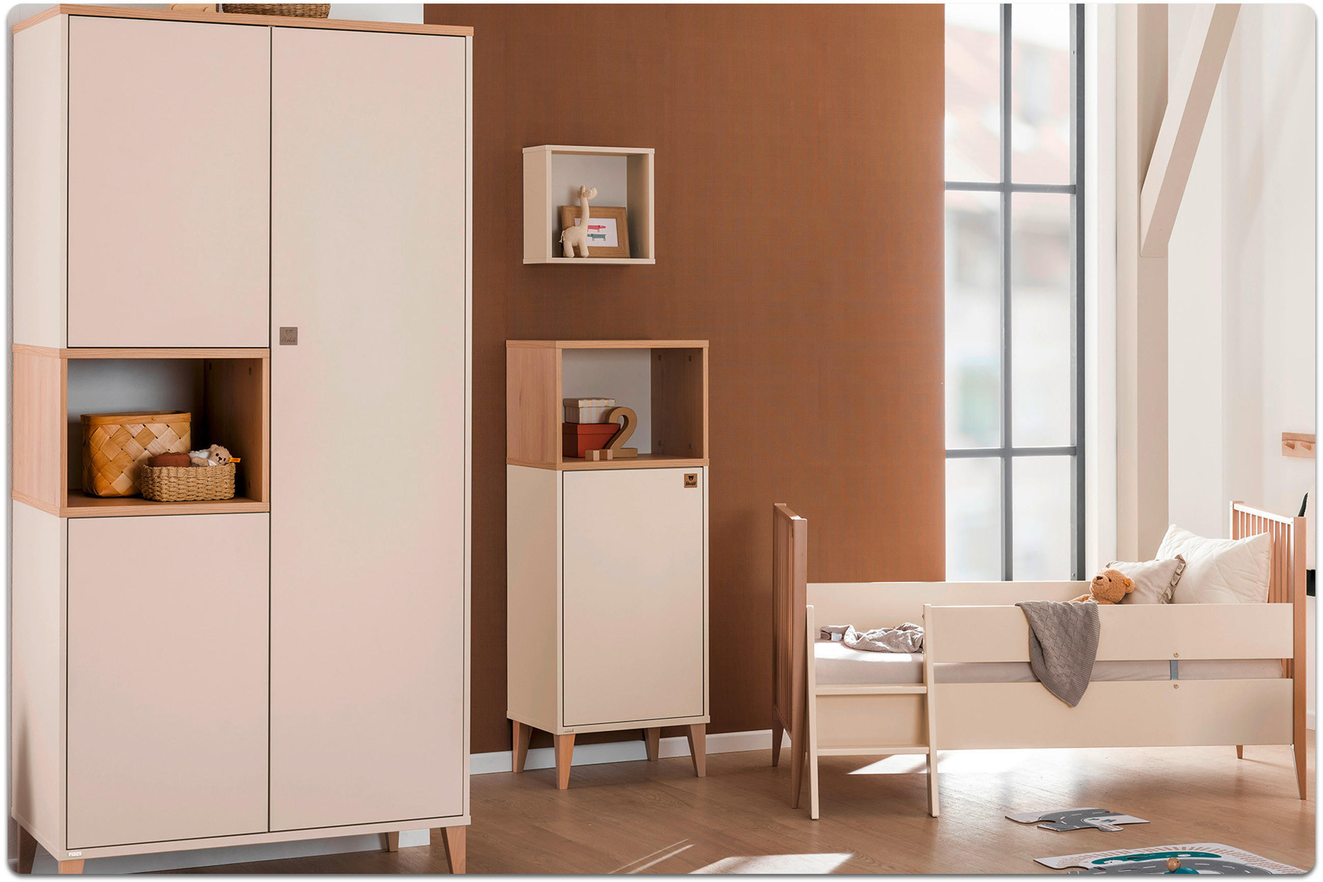 Kinderzimmer mit weißem Schrank, kleinem Sideboard, Kinderbett mit Stofftier und großem Fenster.