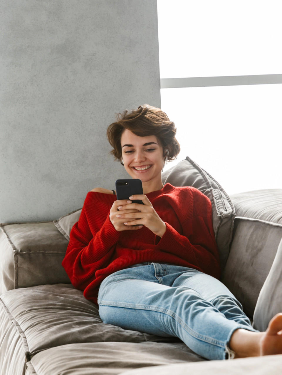 Person som sitter avslappnat i en soffa med en smartphone.