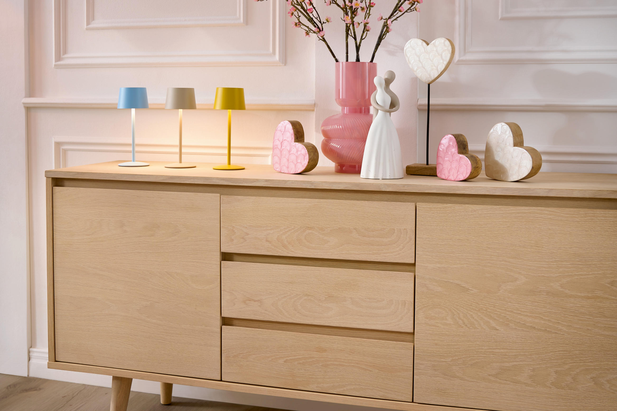 Braune Holzkommode mit weißer und rosa Deko mit Dekoherzen und weißer Wand