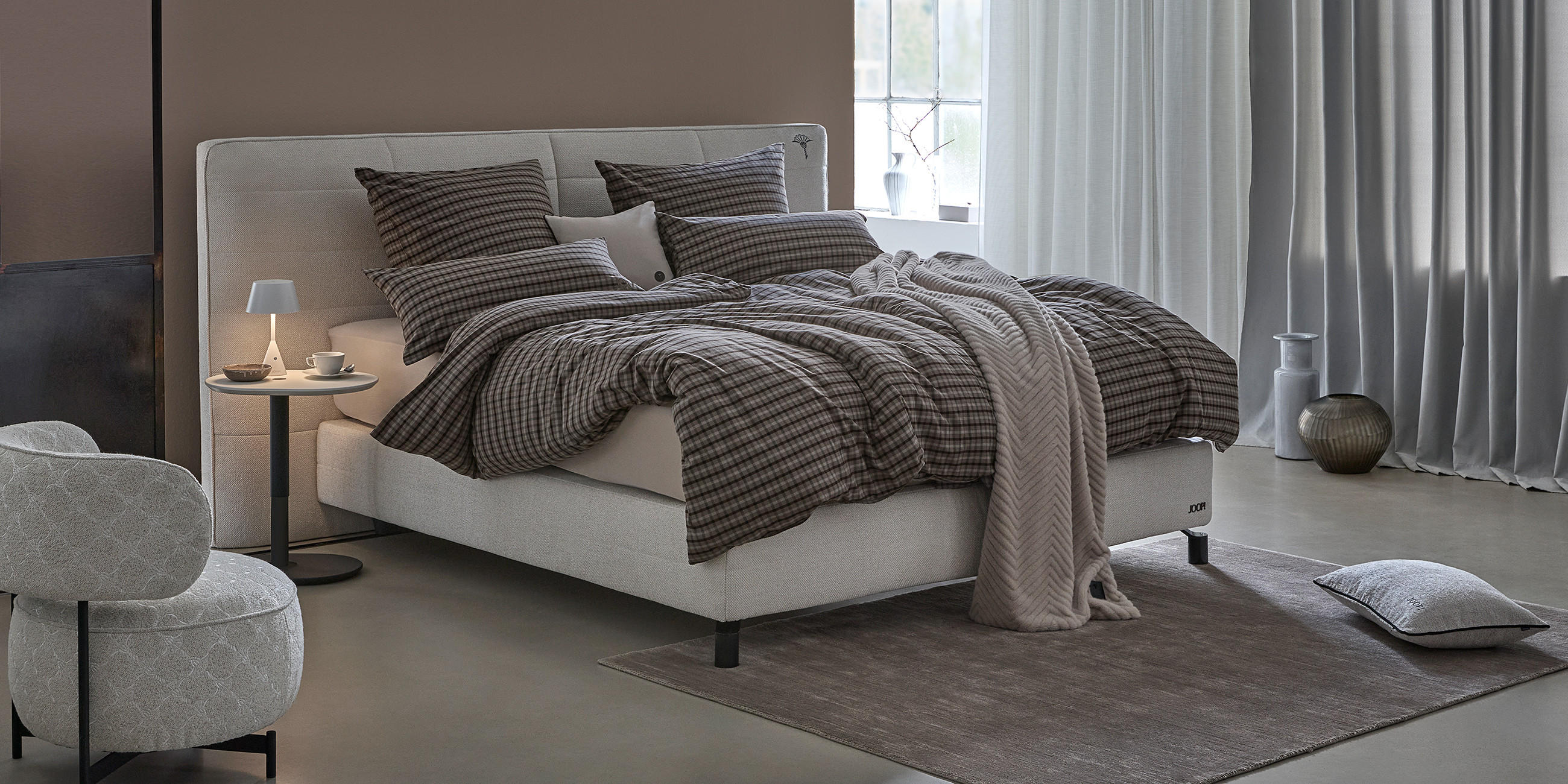 Stimmungsvolle Nachttischleuchte in einem Schlafzimmer mit hochwertigen Produkten der Marke JOOP! Living.