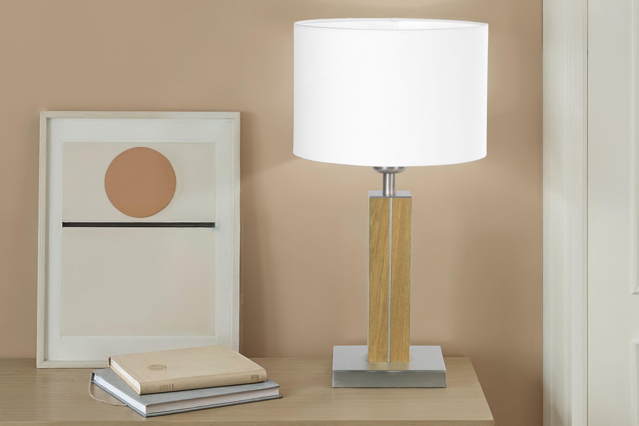 Eine moderne Tischlampe mit großem, weißem Stoffschirm steht auf einem Holz- und Metallfuß auf einem Sideboard neben zwei Büchern.