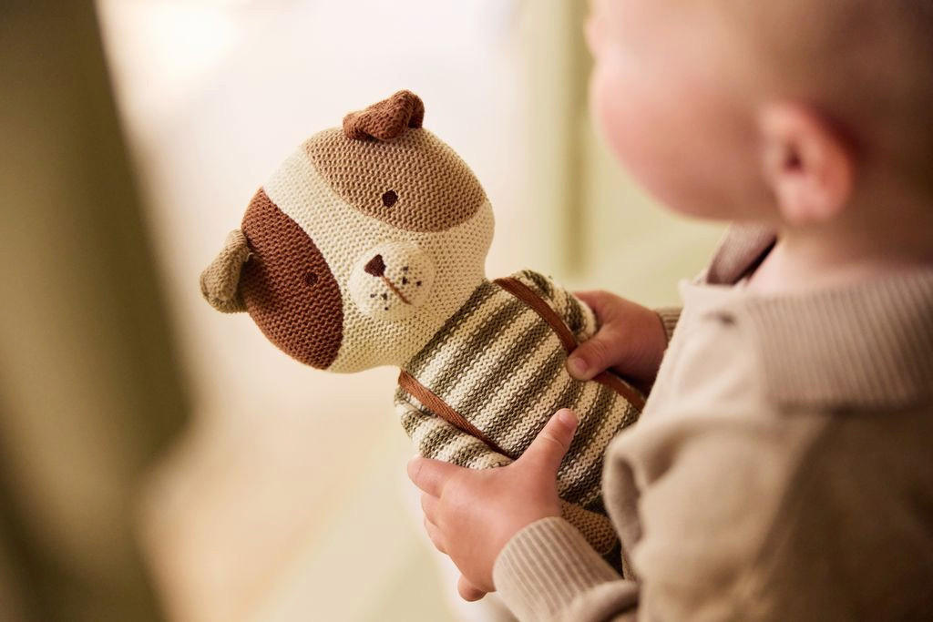 Dojenček se igra s plišasto igračo, ki jo drži v rokah.